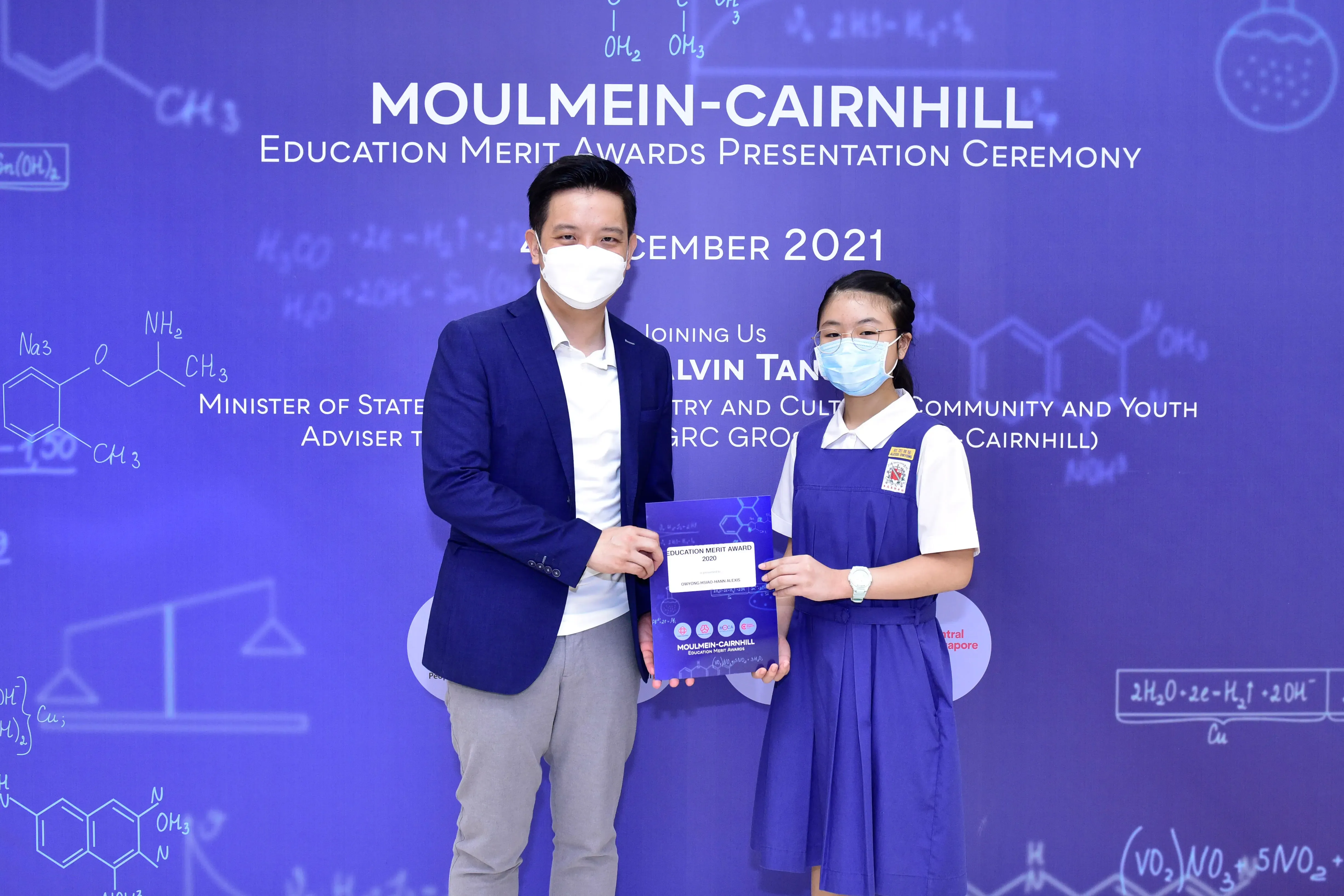 Two masked individuals hold an award certificate at the Moulmein-Cairnhill Education Merit Awards Ceremony, December 2021.