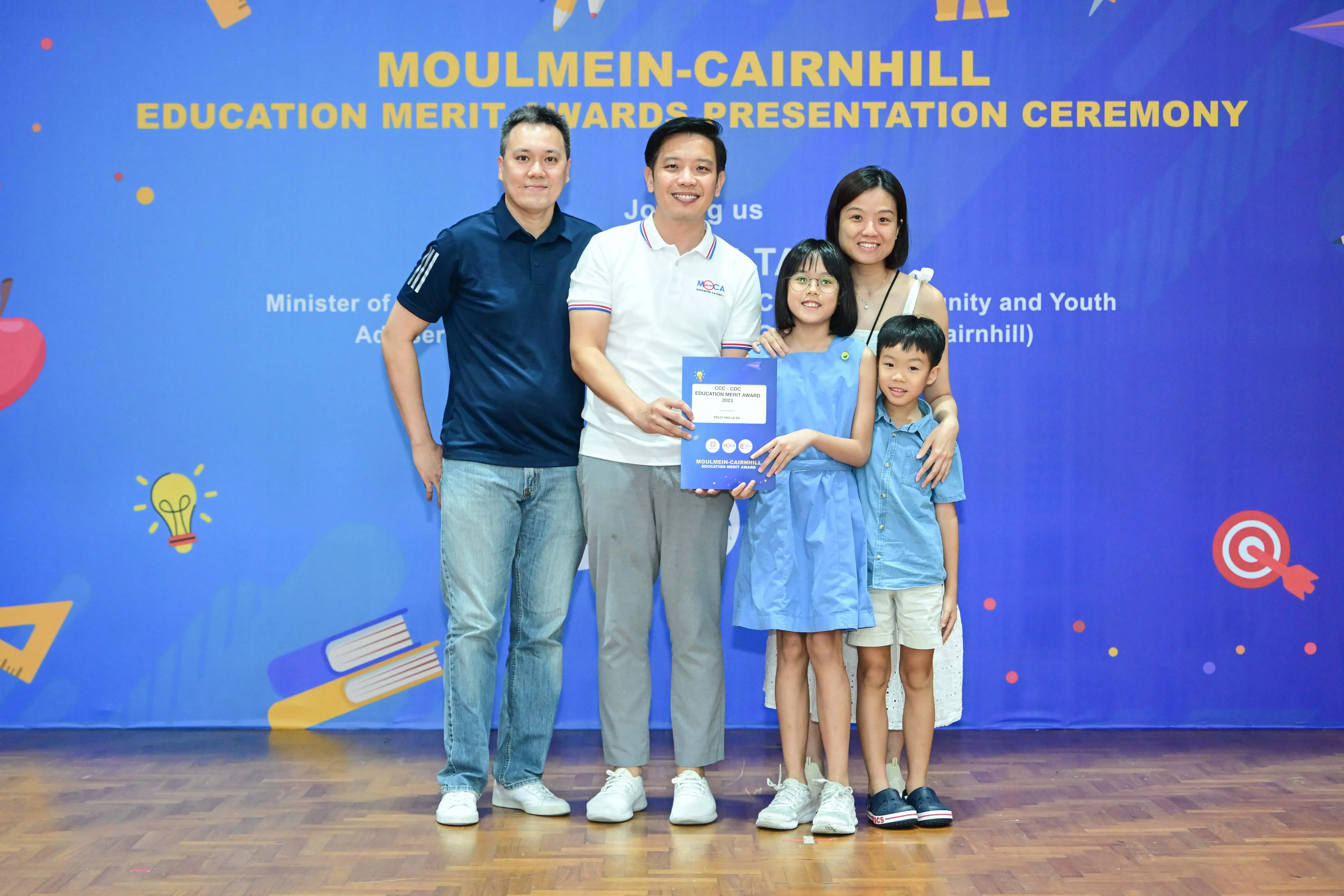 Family of four posing with an award certificate at the Moulmein-Cairnhill Education Merit Awards Presentation Ceremony.