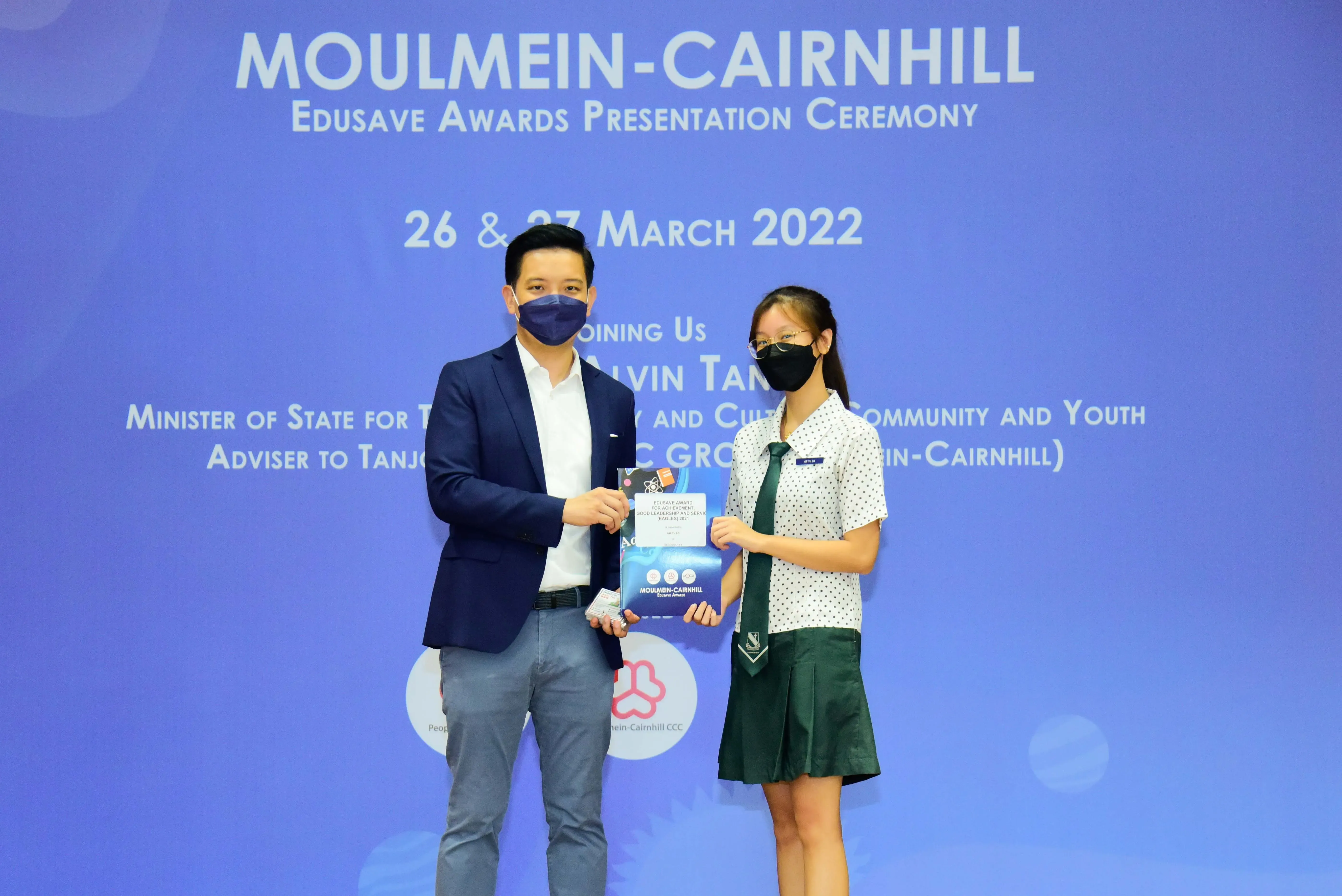 Two masked individuals hold an award at the Moulmein-Cairnhill Edusave Awards Presentation Ceremony, March 2022.