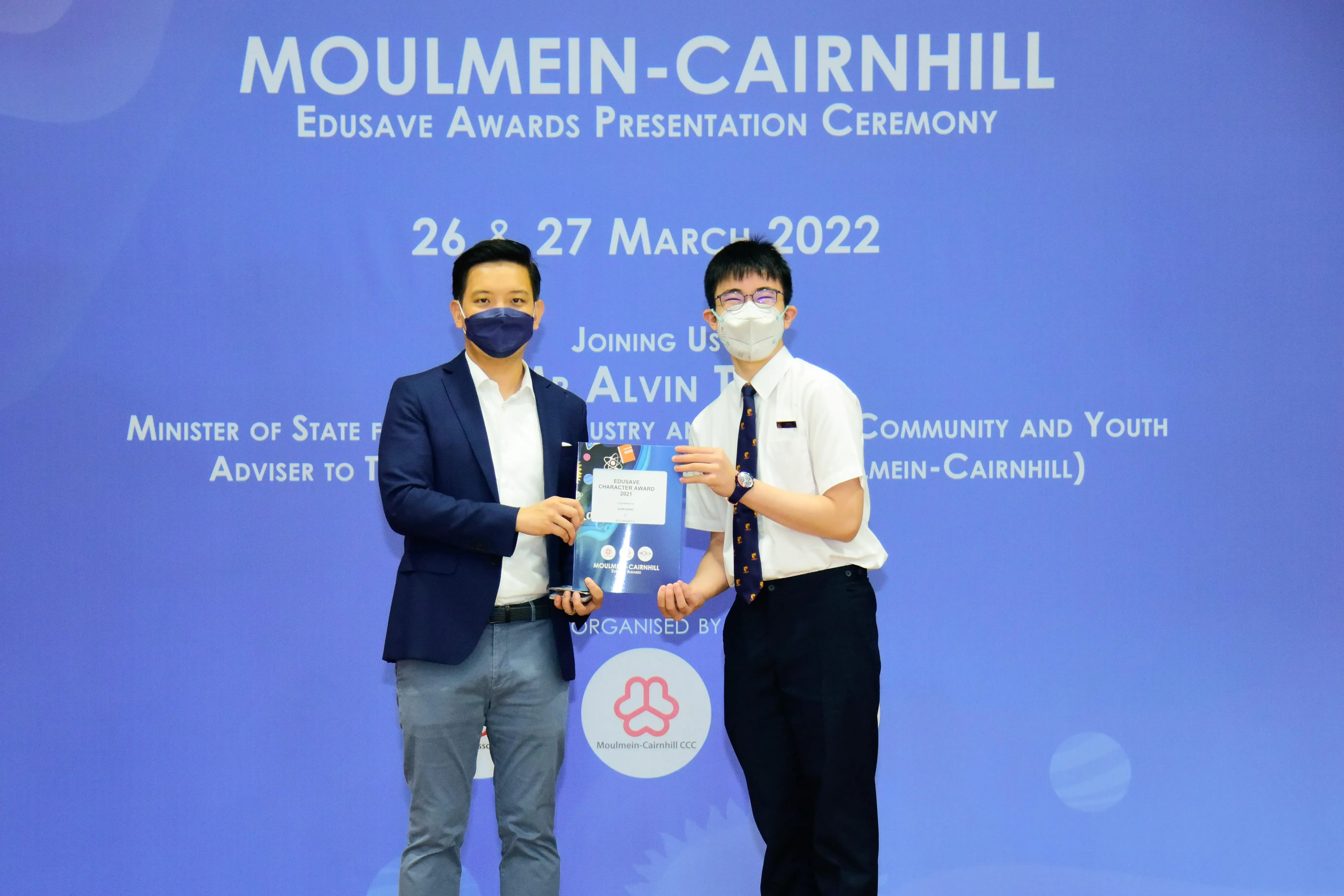 Two masked men hold an award certificate at the Moulmein-Cairnhill Edusave Awards Presentation Ceremony, March 2022.