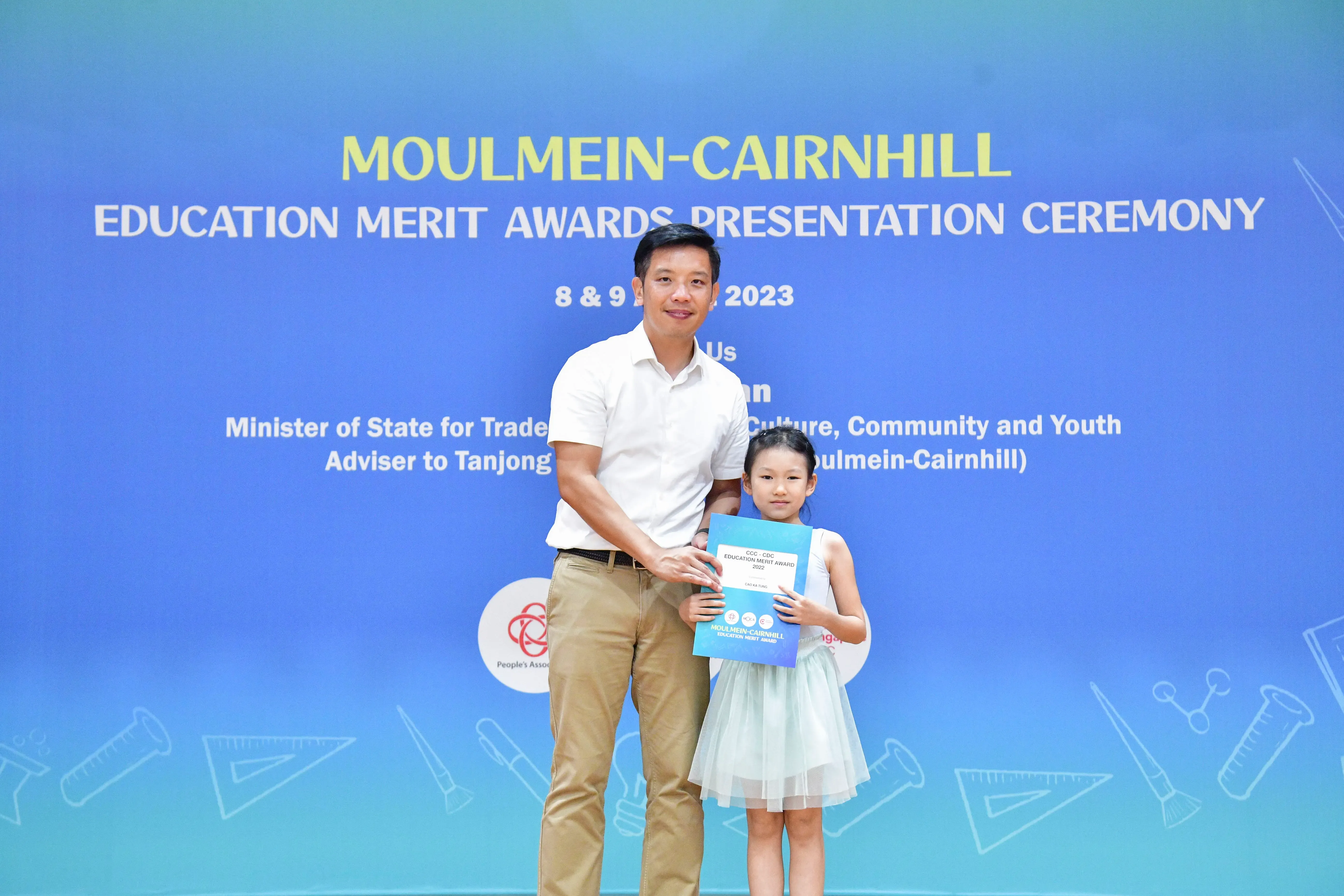 A man and a young girl hold a certificate at the Moulmein-Cairnhill Education Merit Awards Ceremony 2023.
