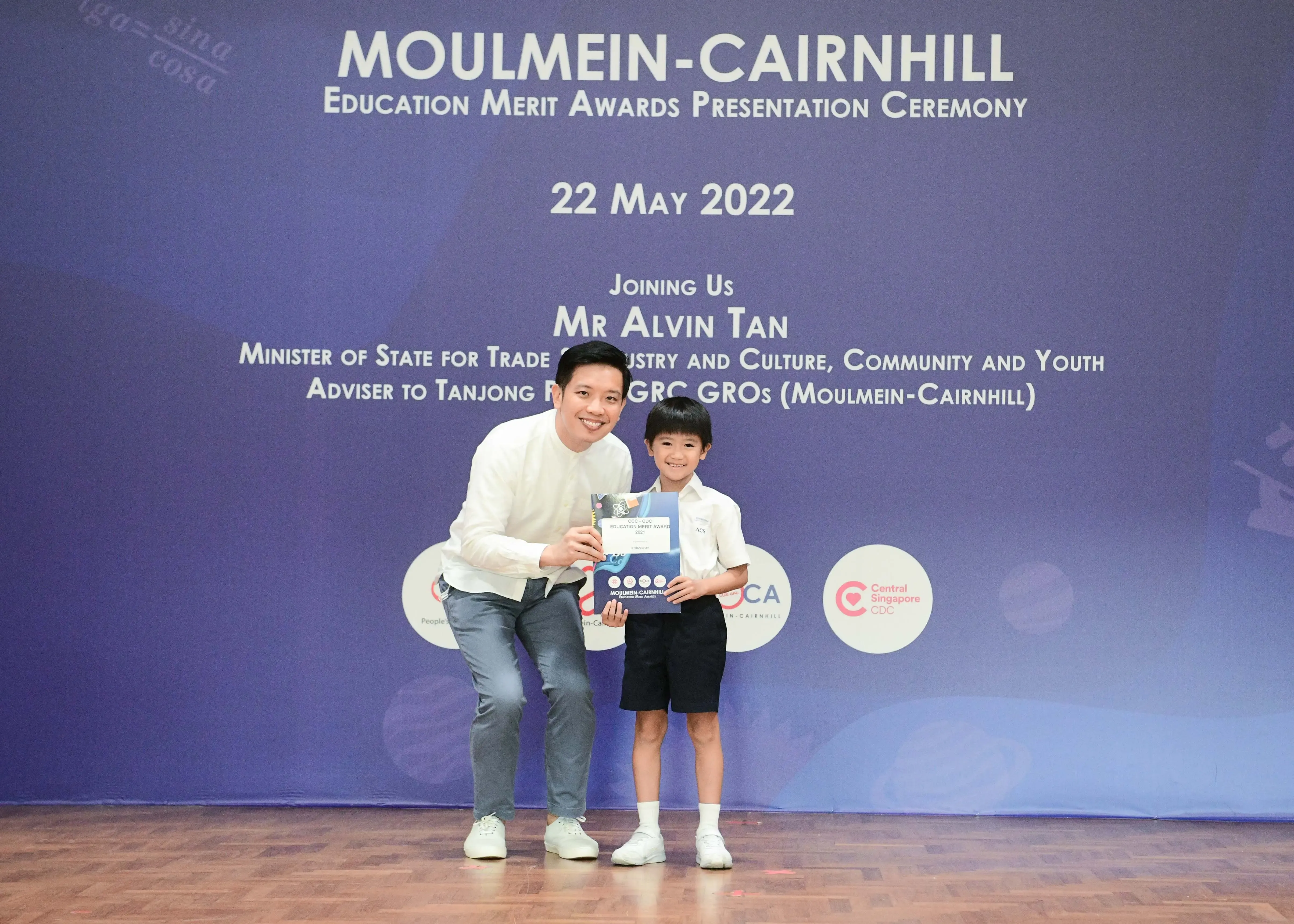 A man and a young boy hold a certificate at the Moulmein-Cairnhill Education Merit Awards Ceremony on 22 May 2022.