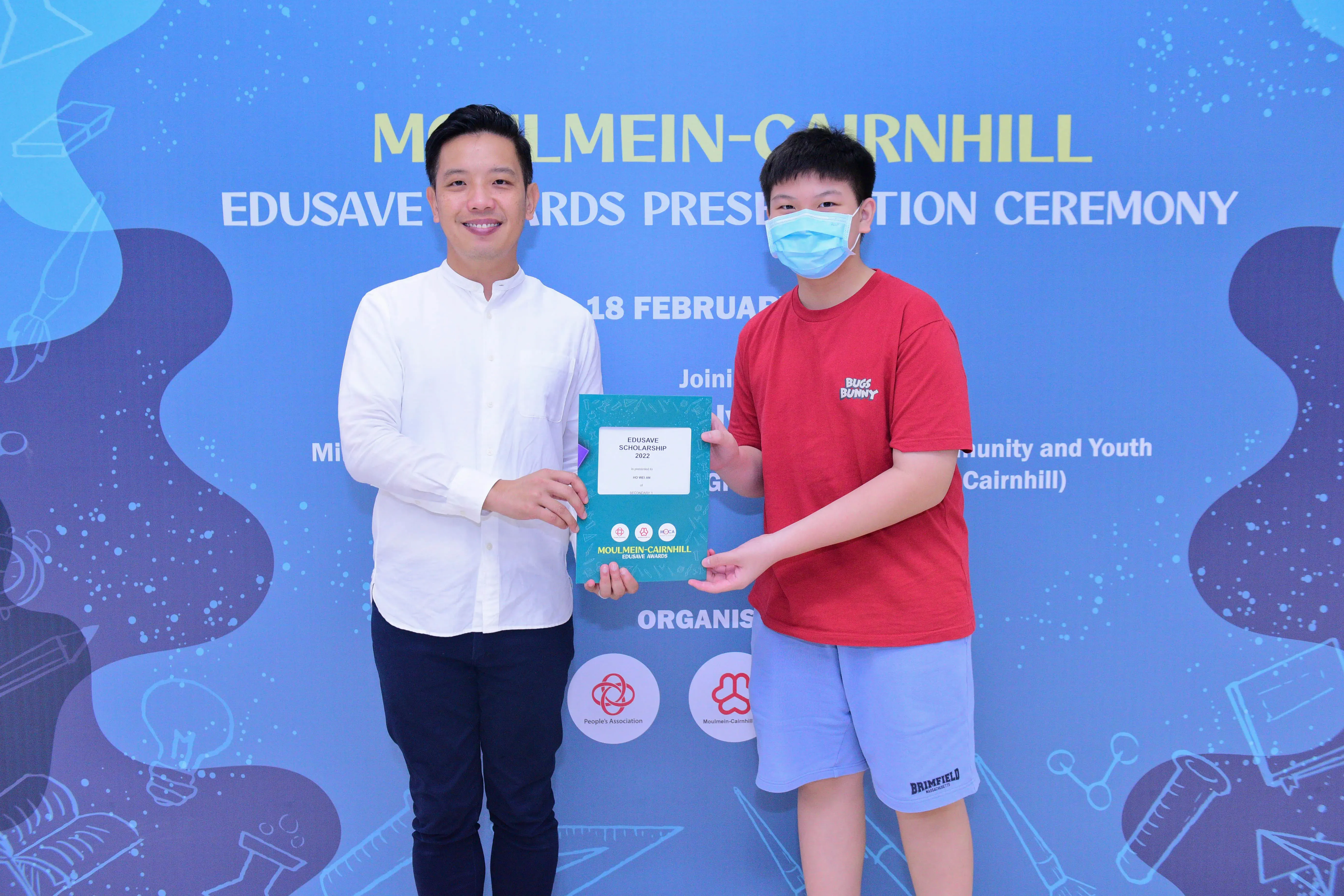 Two people hold an Edusave Scholarship certificate at the Moulmein-Cairnhill Edusave Awards Presentation Ceremony.