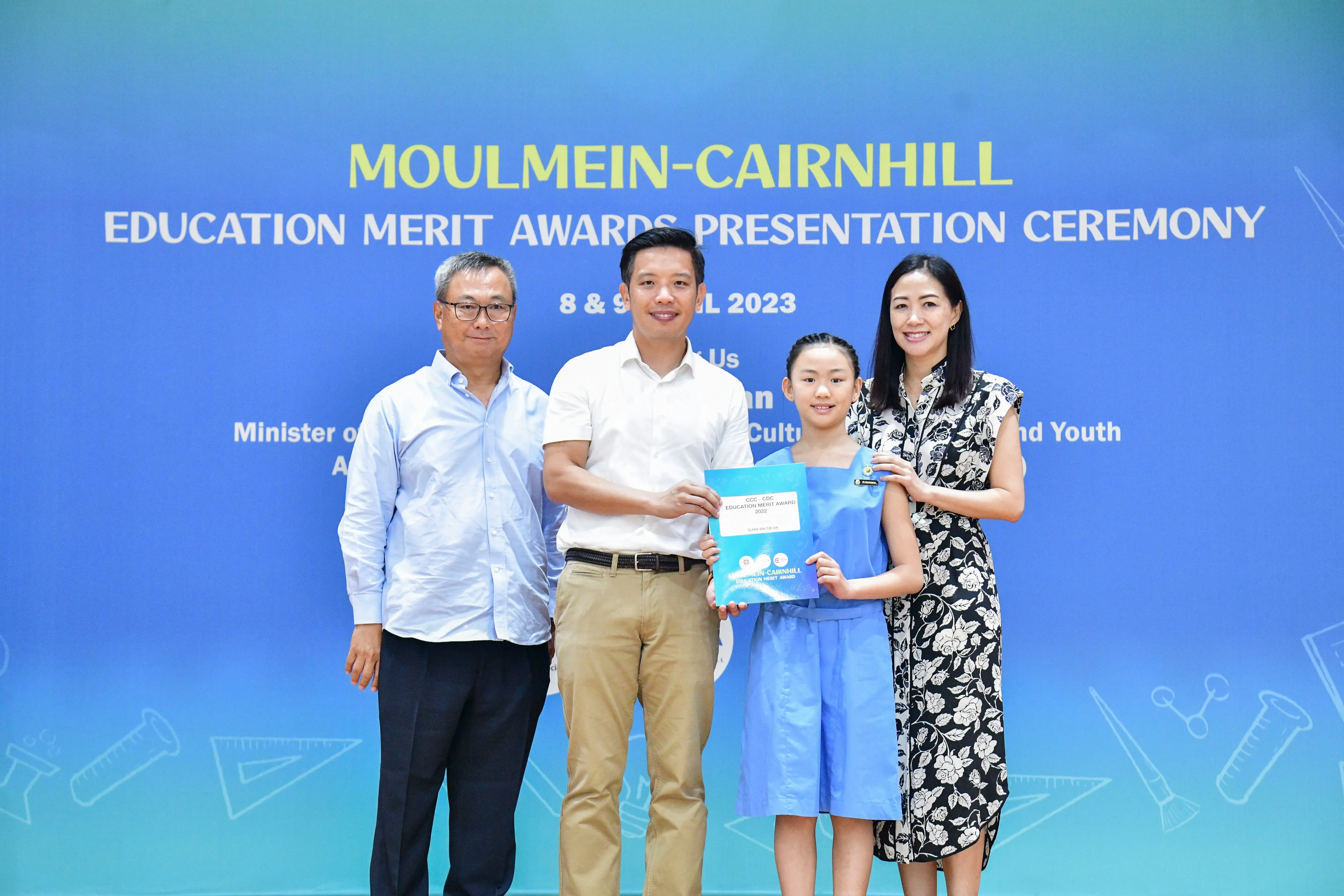 Four people pose at the Moulmein-Cairnhill Education Merit Awards Presentation Ceremony, with a girl holding an award certificate.