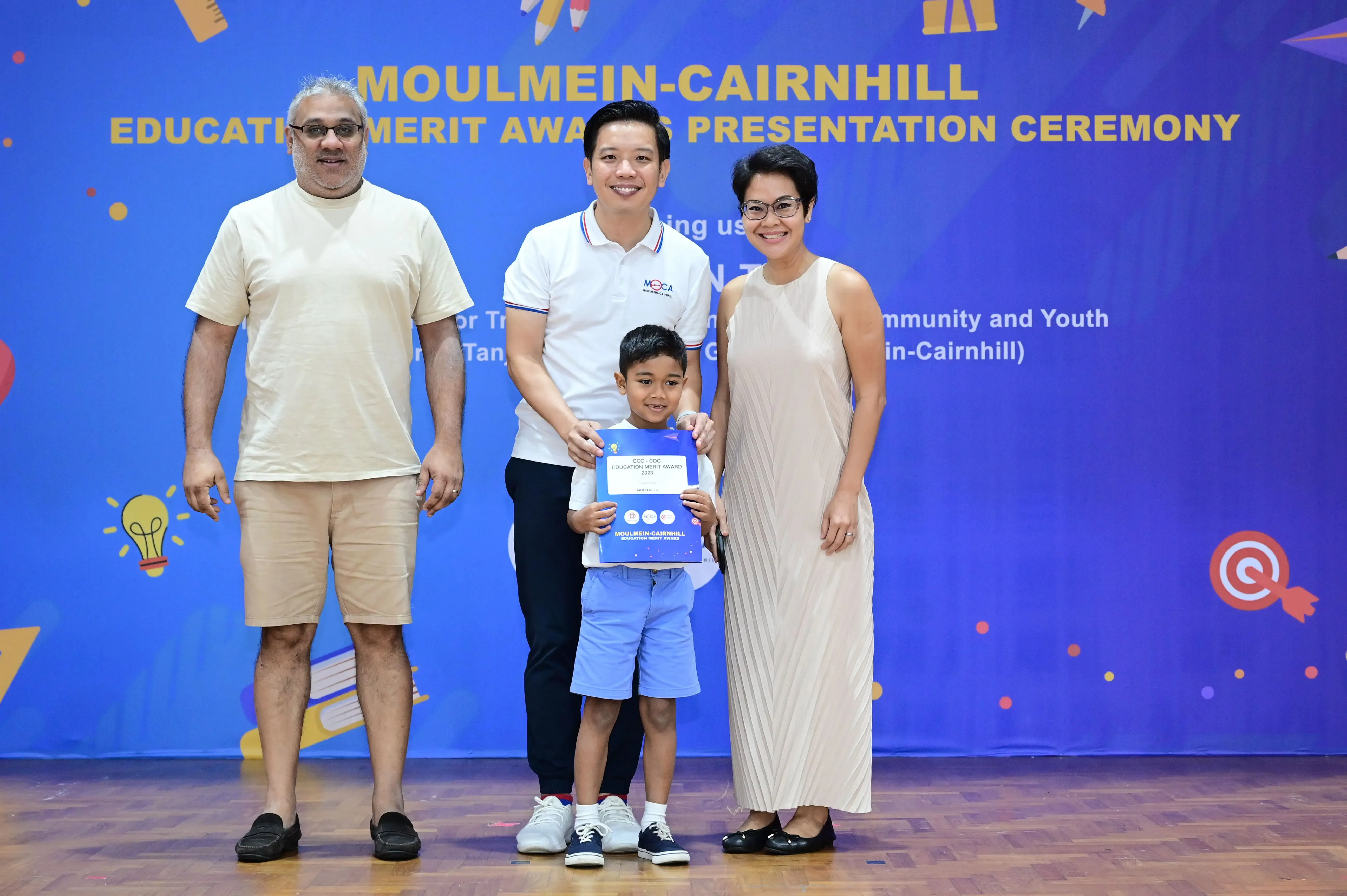 Three adults and a young boy holding a blue Education Merit Award certificate at the Moulmein-Cairnhill ceremony.