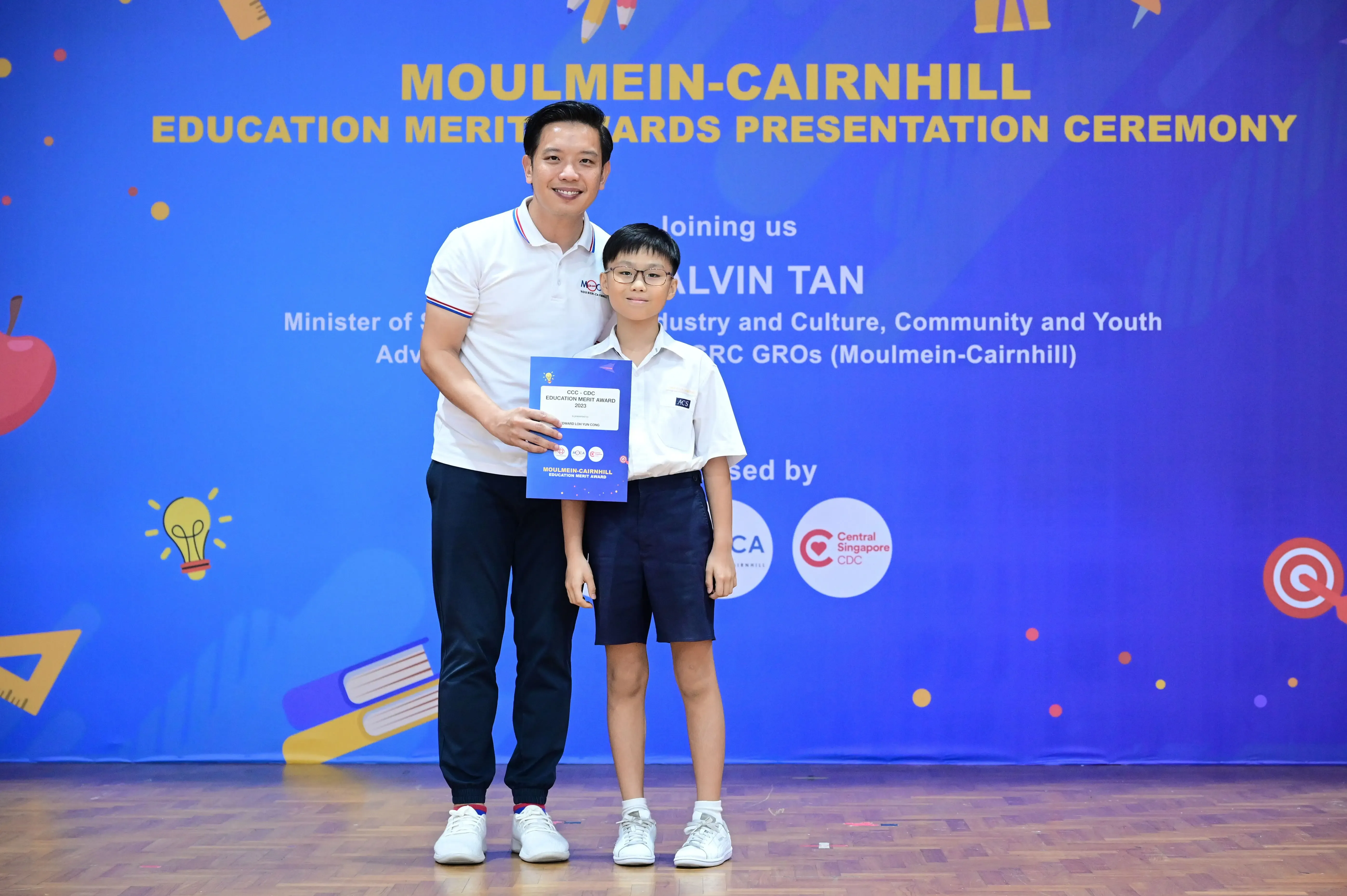 An adult and a young boy hold a certificate at the Moulmein-Cairnhill Education Merit Awards Presentation Ceremony.