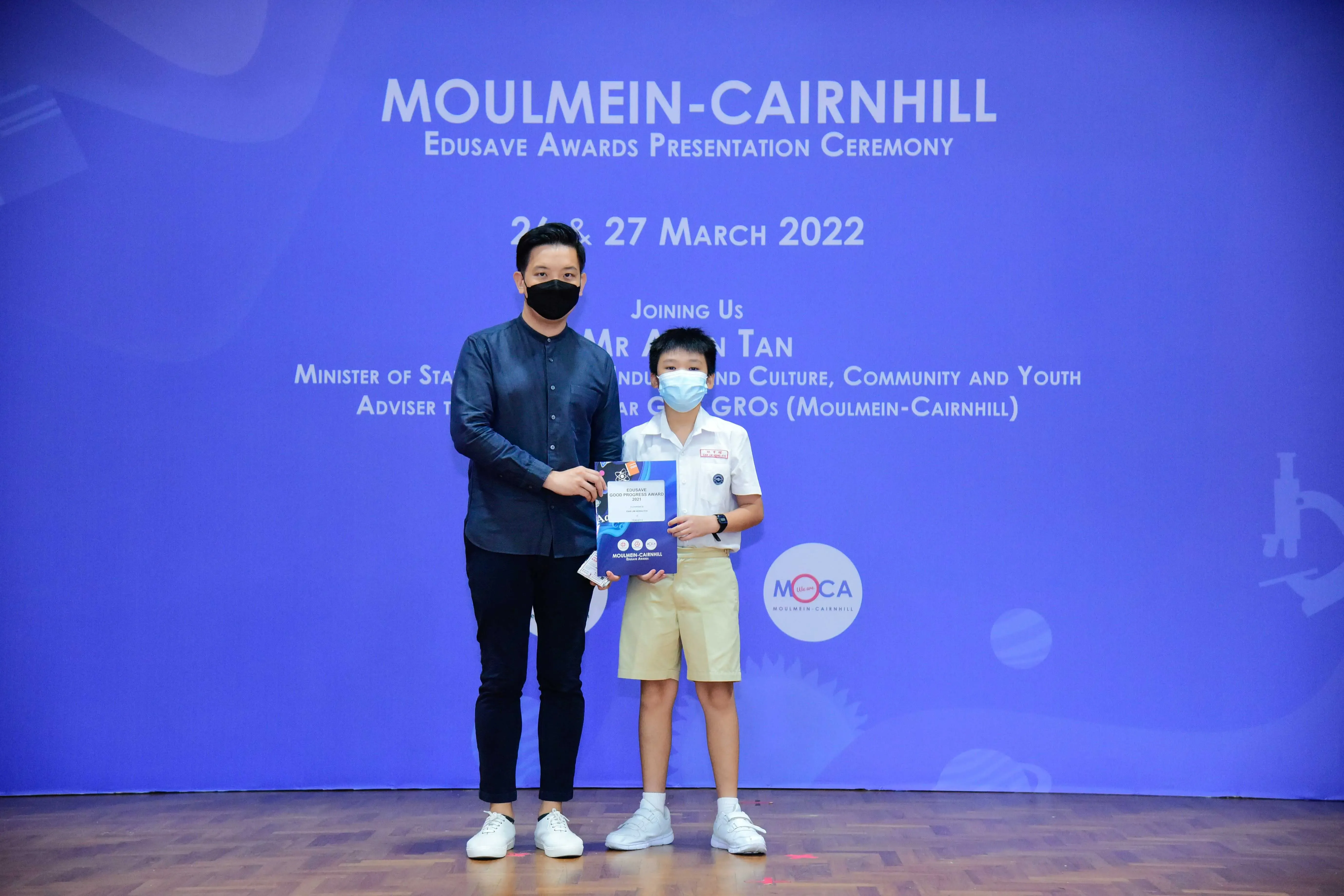 An adult and a young student in uniform hold an award certificate at the Moulmein-Cairnhill Edusave Awards Ceremony 2022.