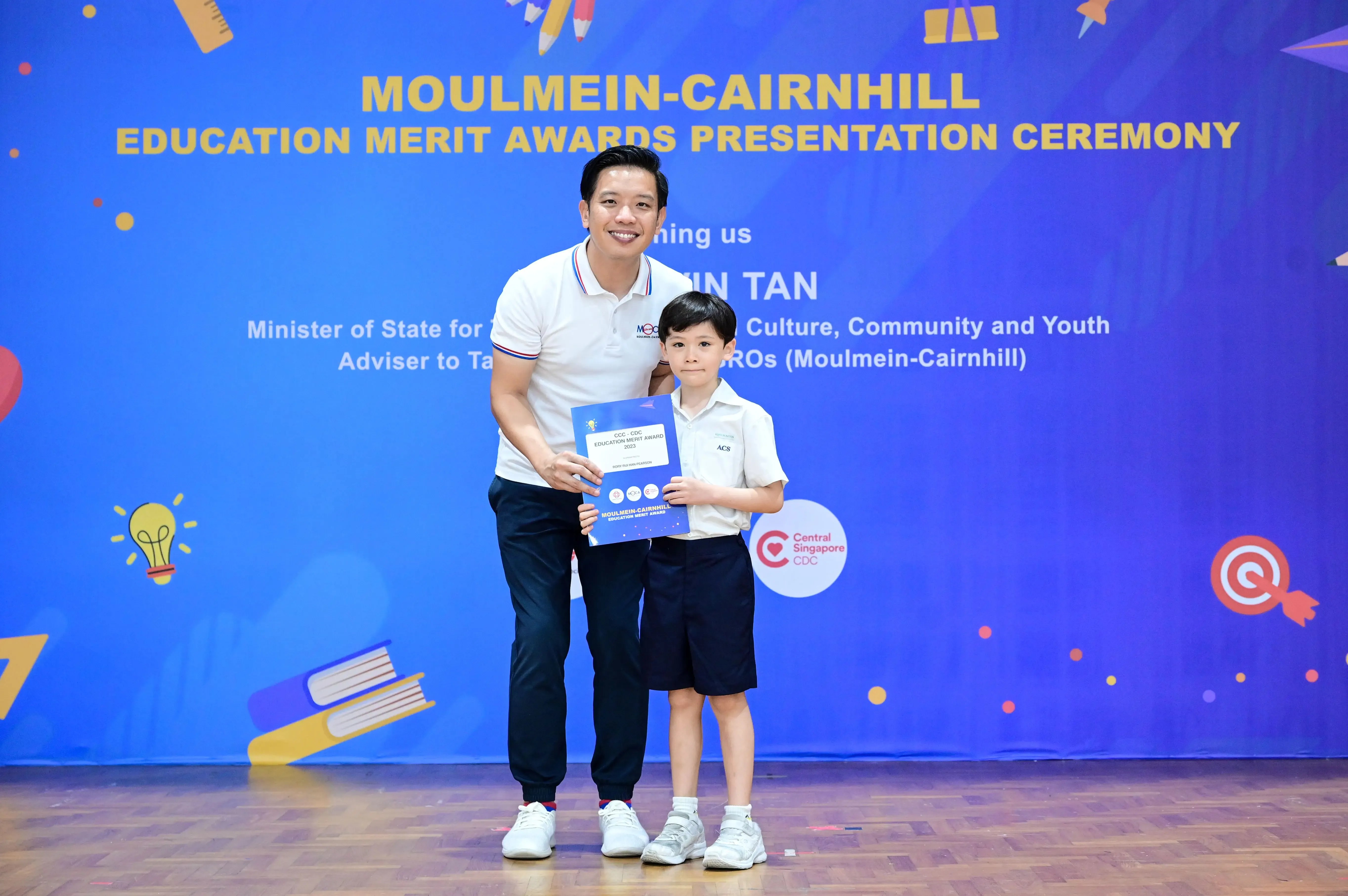 A man and a young boy hold a certificate at the Moulmein-Cairnhill Education Merit Awards Presentation Ceremony.