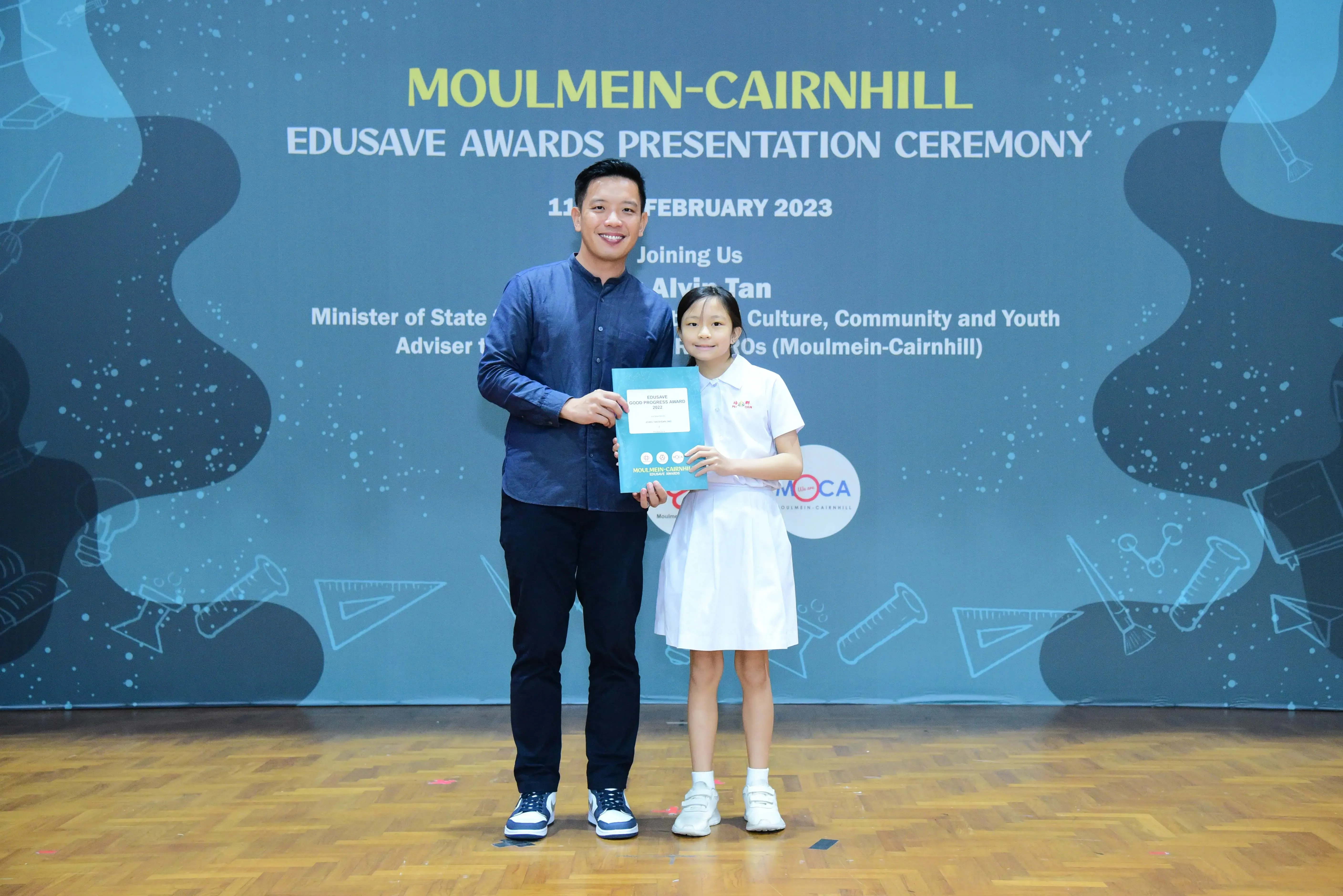 A man and a young girl hold a certificate at the Moulmein-Cairnhill Edusave Awards Presentation Ceremony, February 2023.