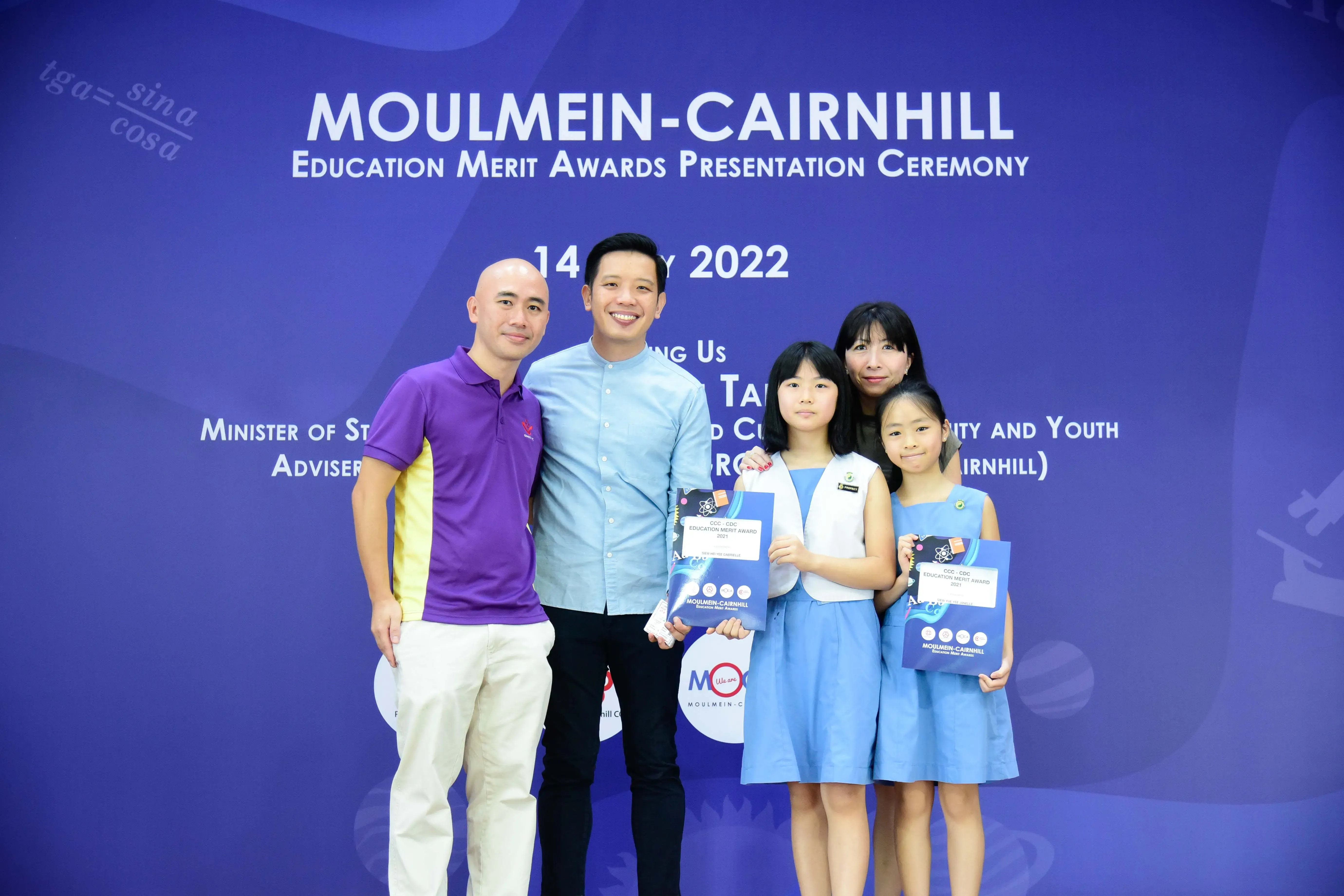 Five people pose at the Moulmein-Cairnhill Education Merit Awards Ceremony on 14 July 2022, two girls holding award folders.