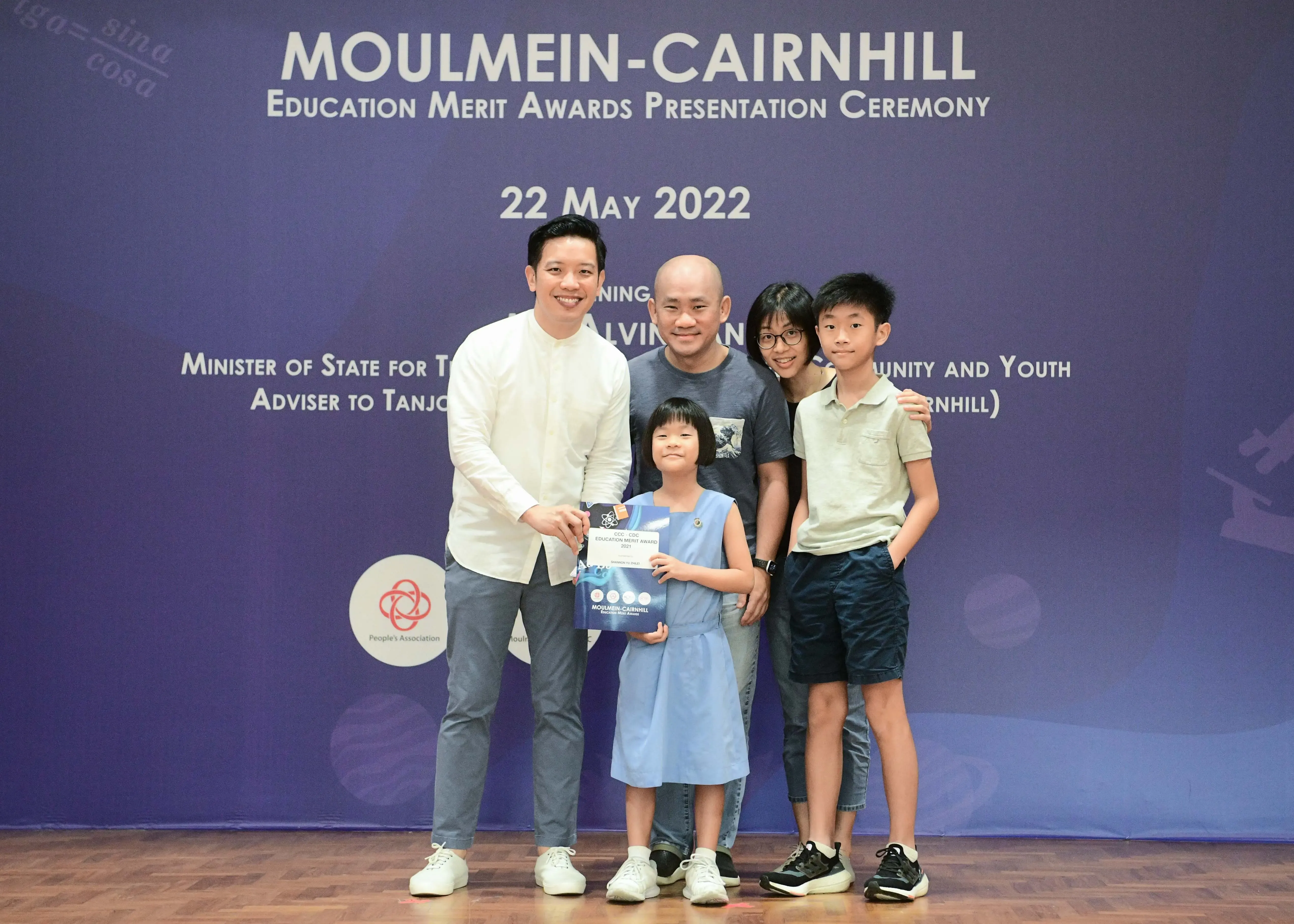 Five people pose at the Moulmein-Cairnhill Education Merit Awards Ceremony on 22 May 2022, with a girl holding a certificate.