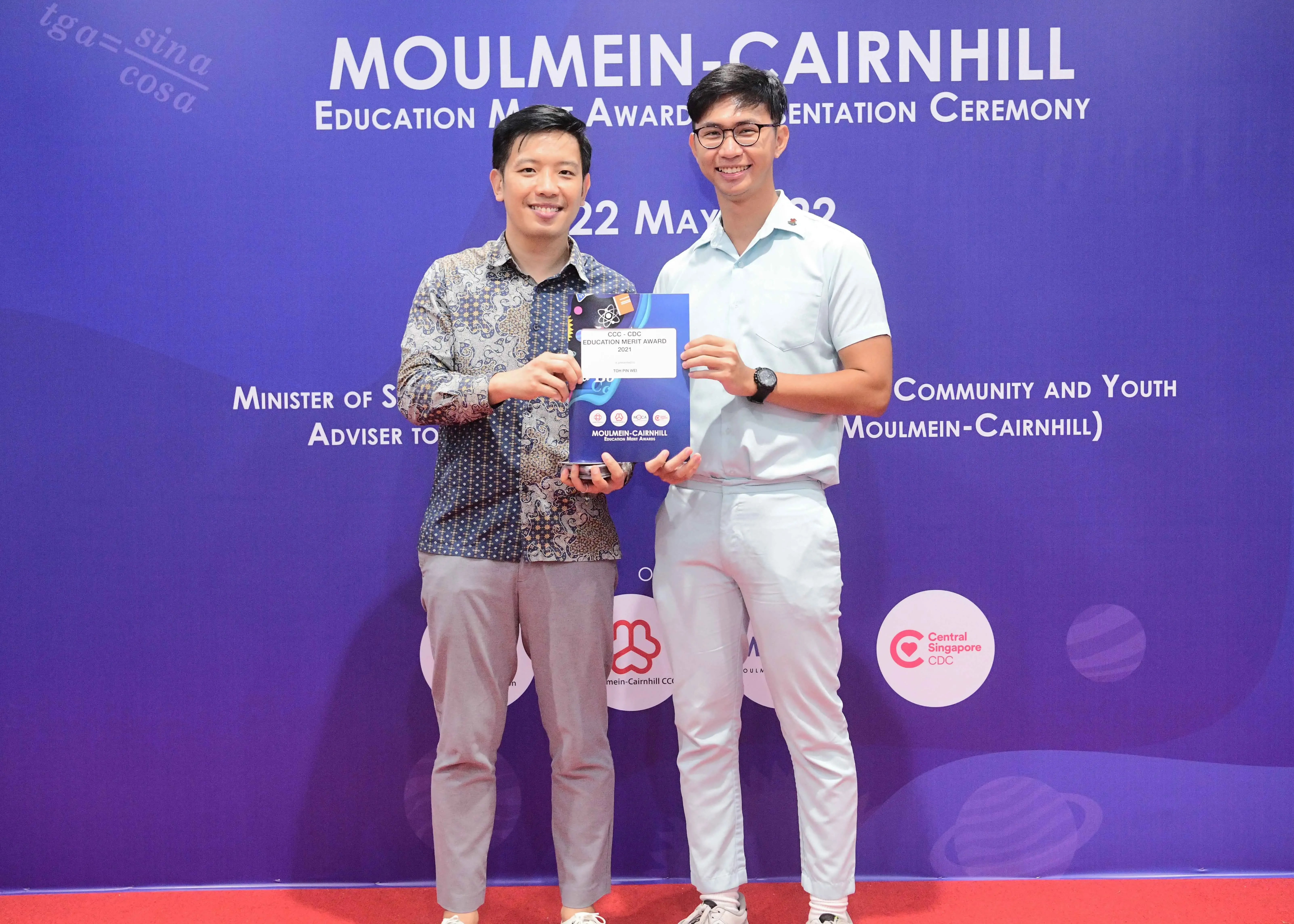 Two men smiling and holding an award at the Moulmein-Cairnhill Education Merit Award Presentation Ceremony.