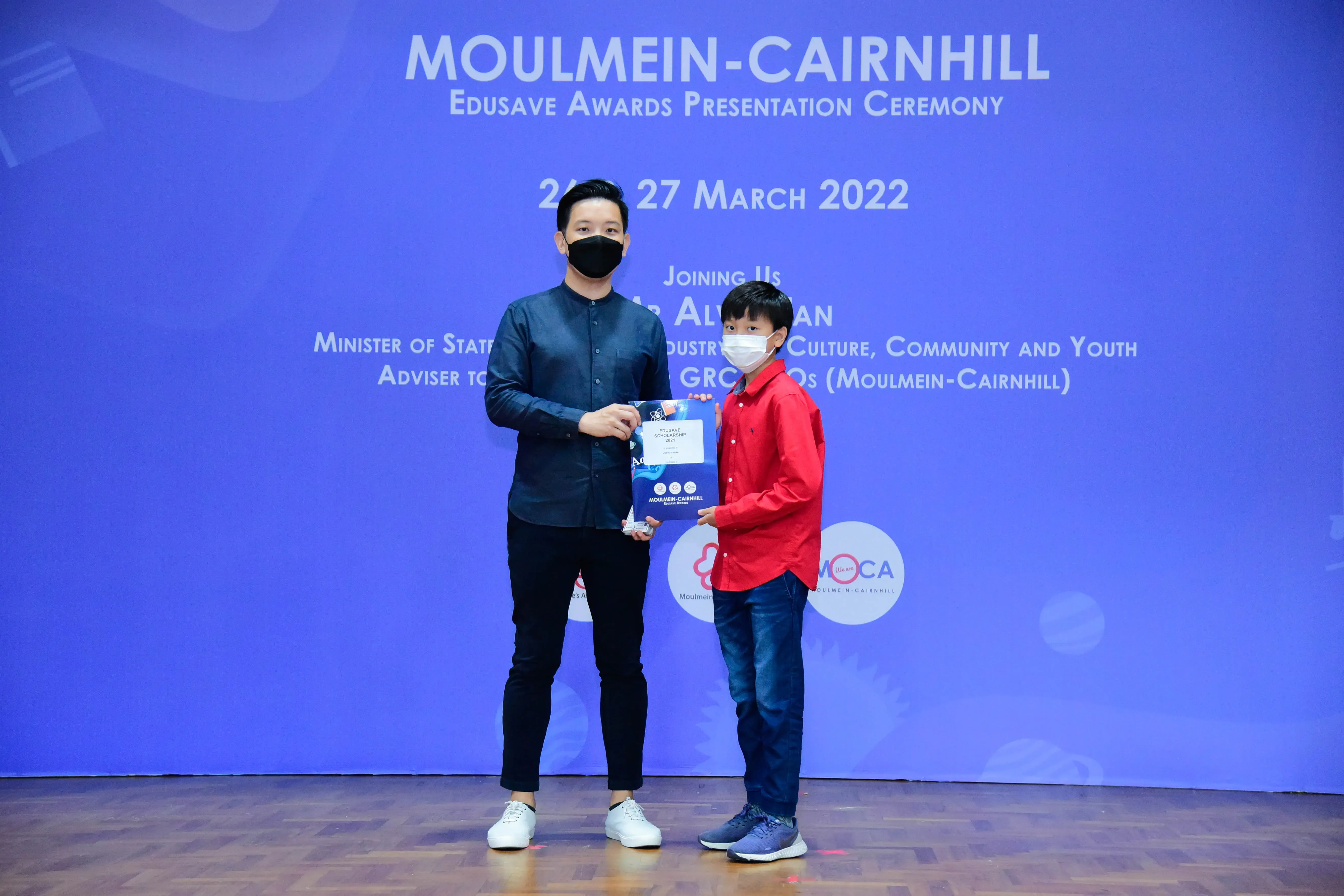 An adult and a child in face masks hold an award certificate at the Moulmein-Cairnhill Edusave Awards Ceremony 2022.