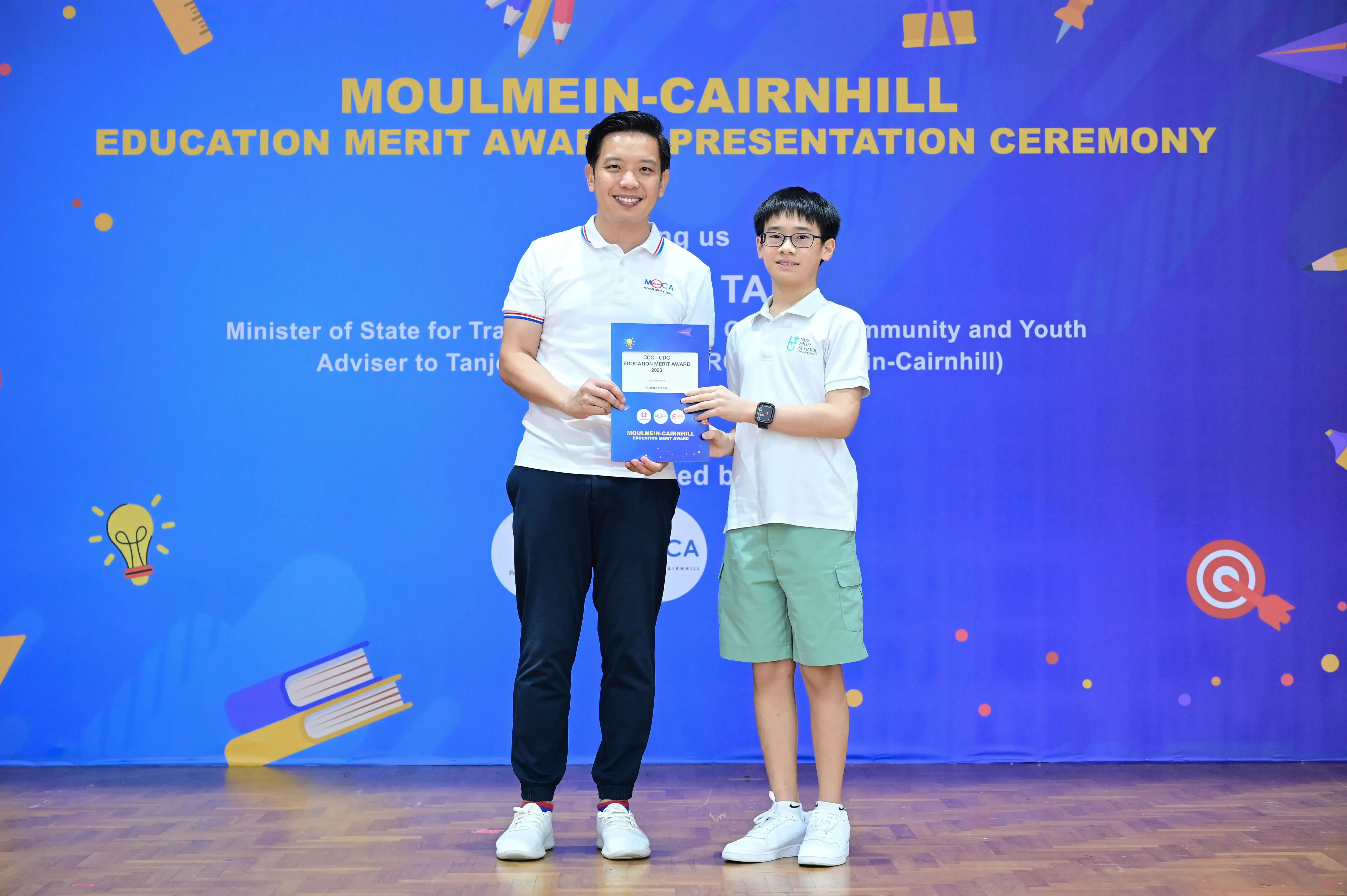 A man and a young boy hold a certificate together at the Moulmein-Cairnhill Education Merit Award Presentation Ceremony.