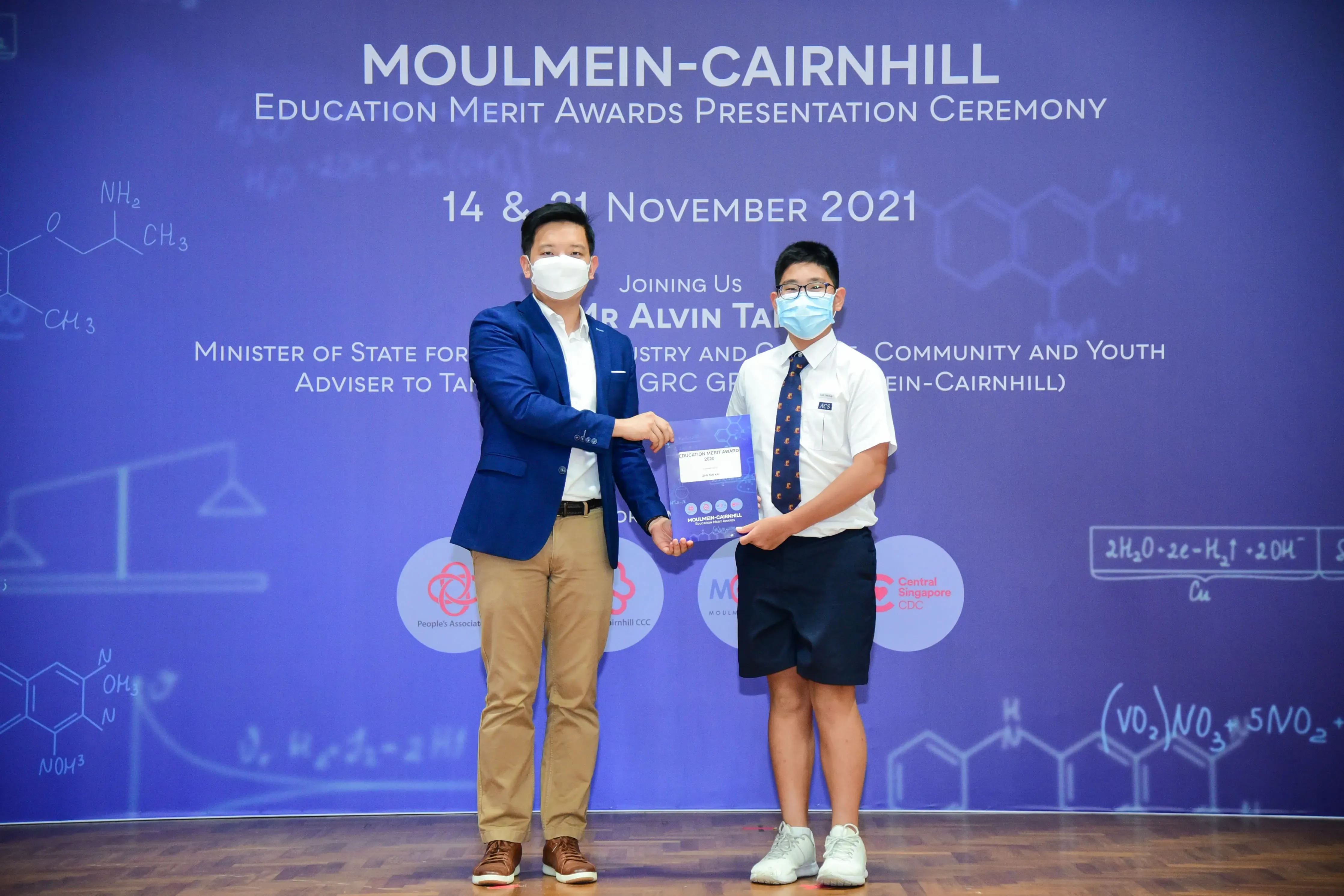 Two masked individuals exchange an award at the Moulmein-Cairnhill Education Merit Awards Ceremony, November 2021.