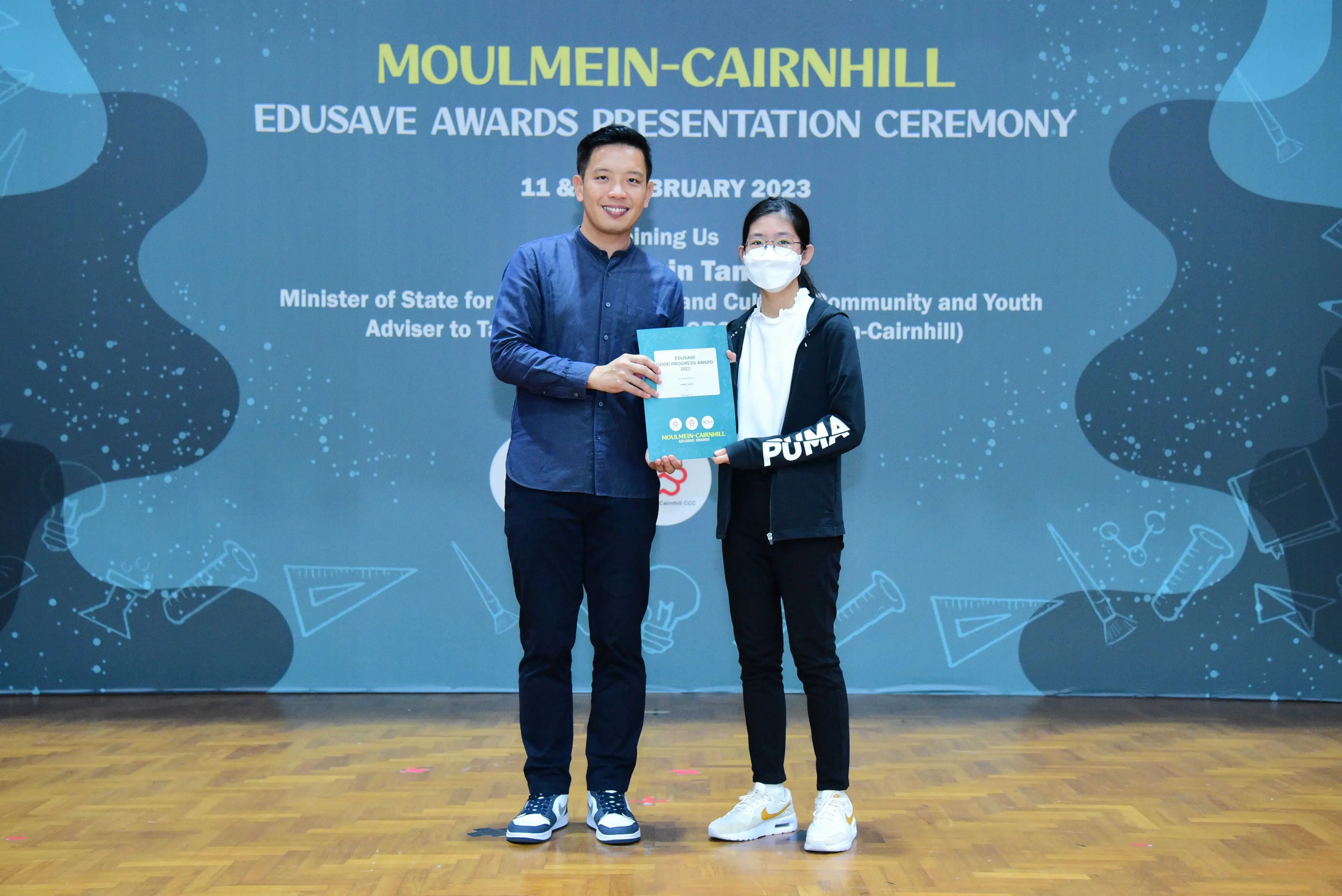 Two people hold a certificate together at the Moulmein-Cairnhill Edusave Awards Presentation Ceremony, February 2023.