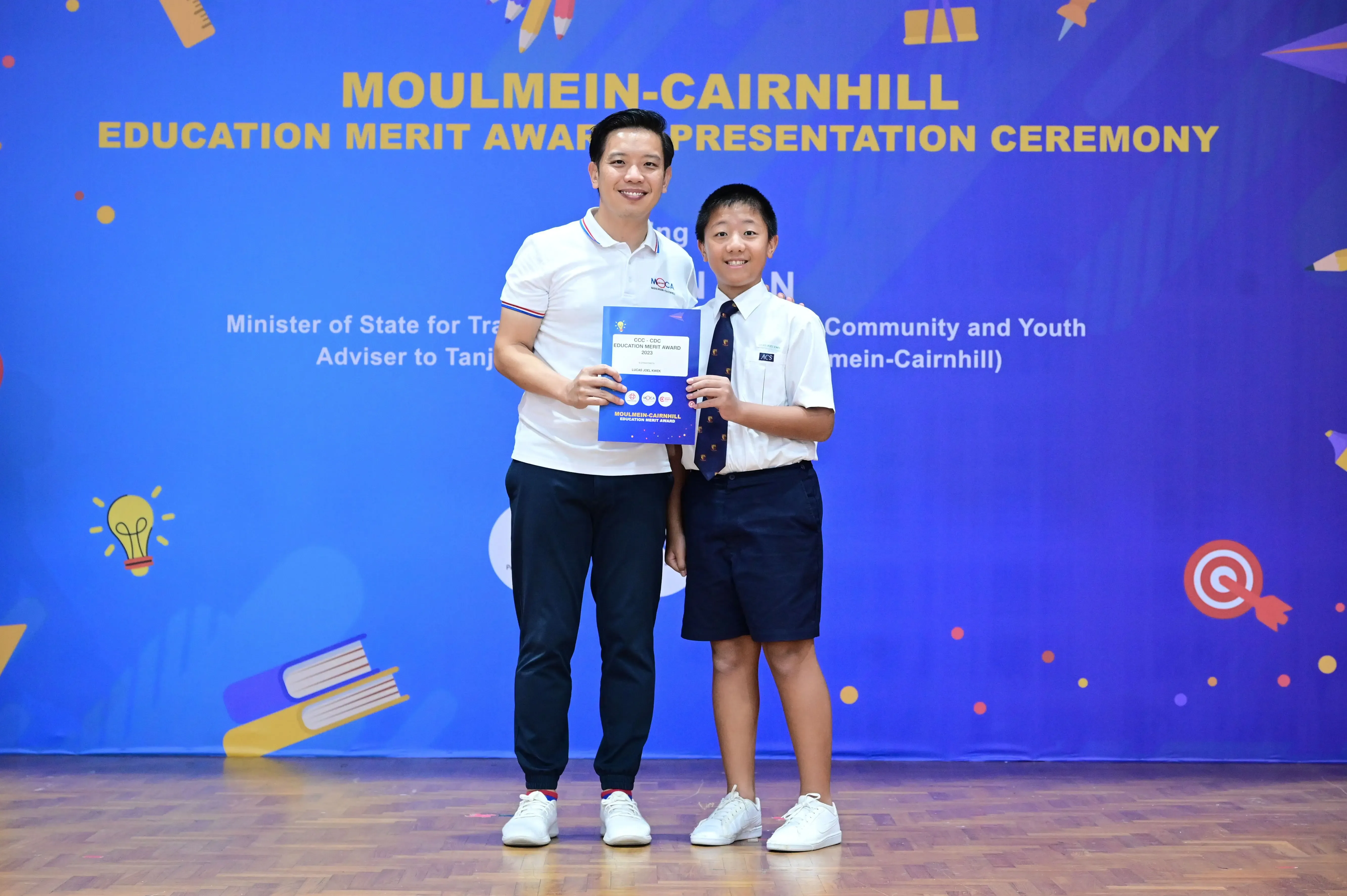 An adult and a young boy hold an award certificate at the Moulmein-Cairnhill Education Merit Award Presentation Ceremony.