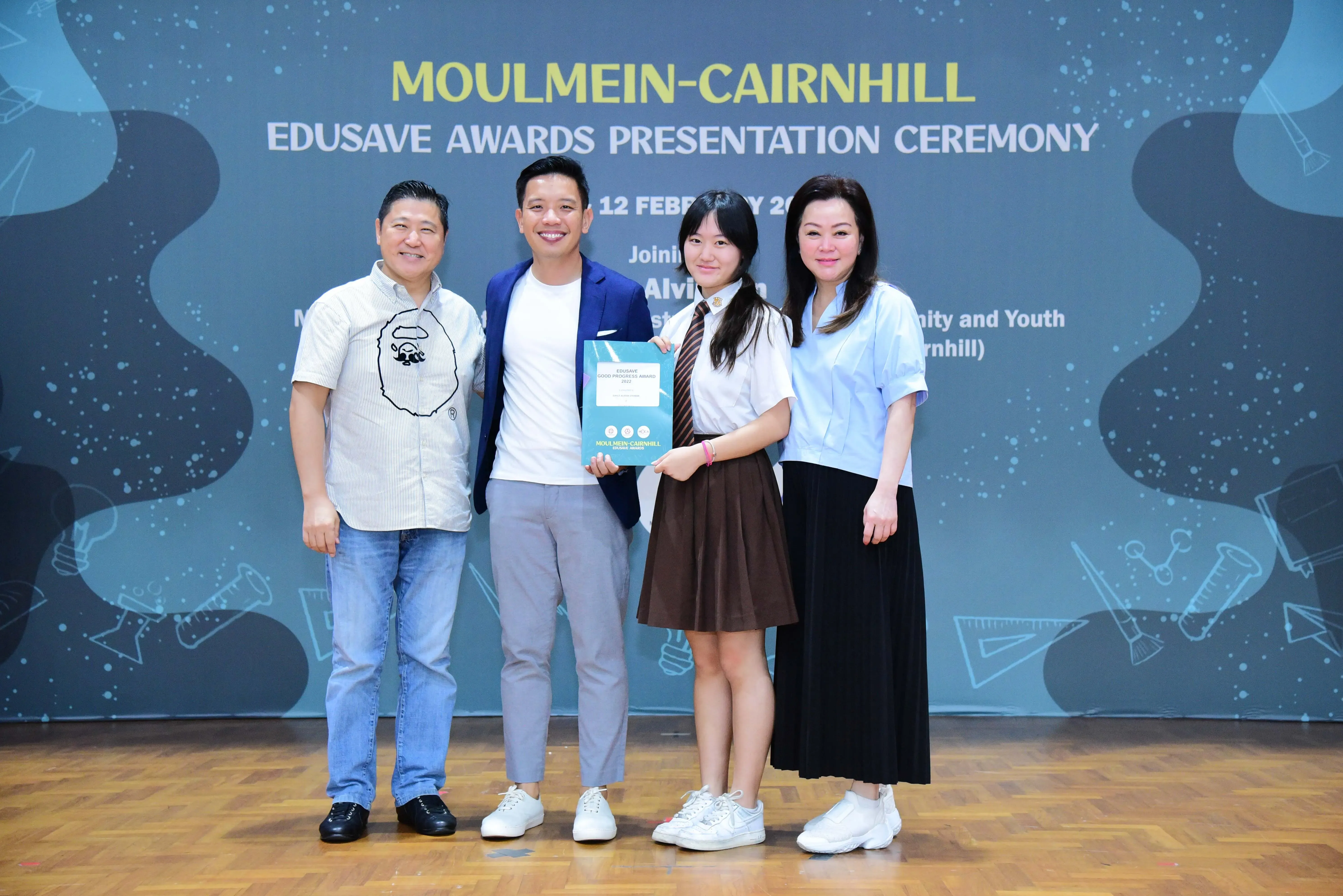 Four people pose at the Moulmein-Cairnhill Edusave Awards Presentation Ceremony, with a student holding a certificate.