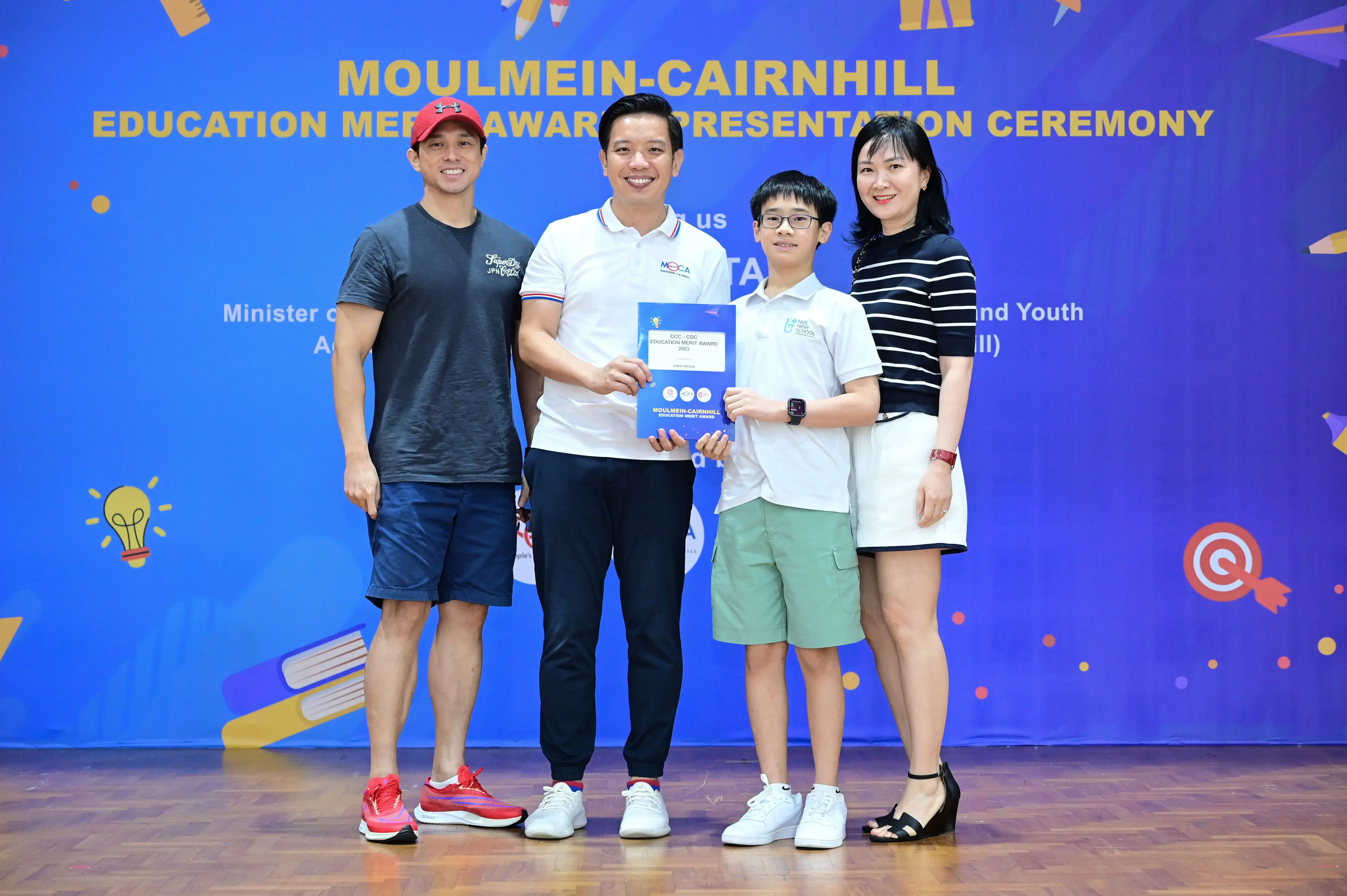 Four people pose together at the Moulmein-Cairnhill Education Merit Award Presentation Ceremony, with a boy holding an award certificate.