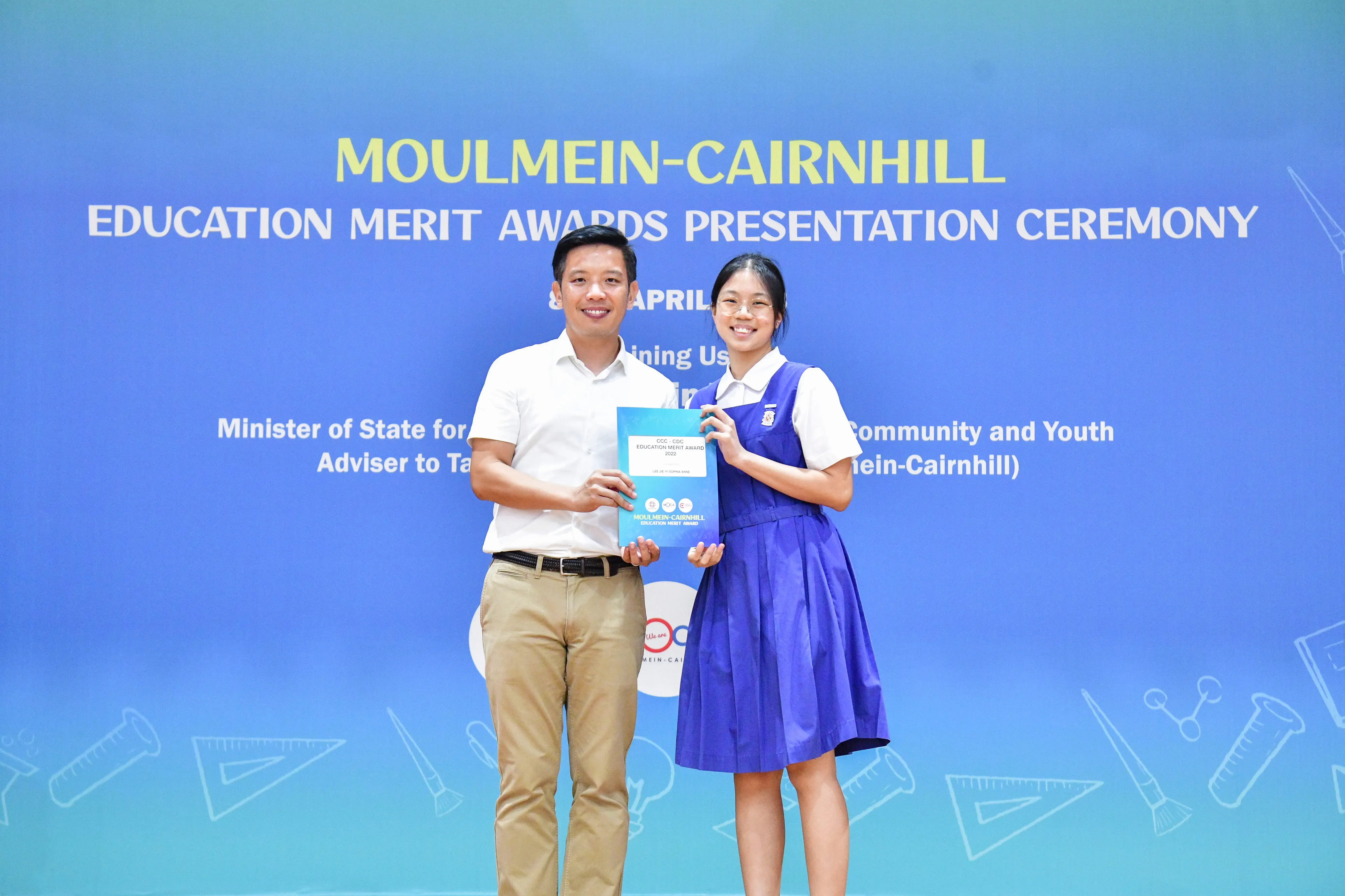 A man and a girl in school uniform hold an award certificate at the Moulmein-Cairnhill Education Merit Awards ceremony.