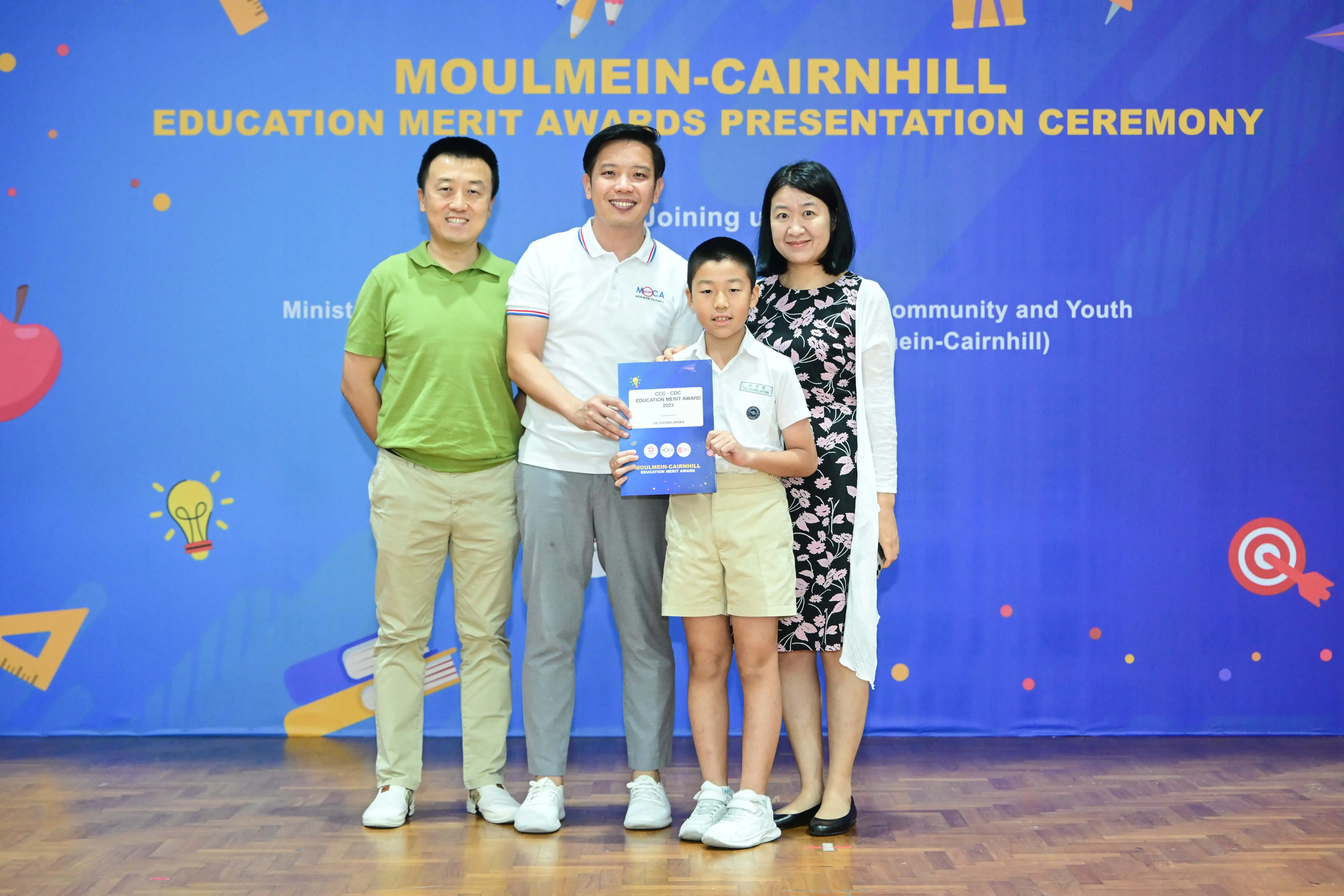 Three adults and a boy pose holding an award certificate at the Moulmein-Cairnhill Education Merit Awards ceremony.