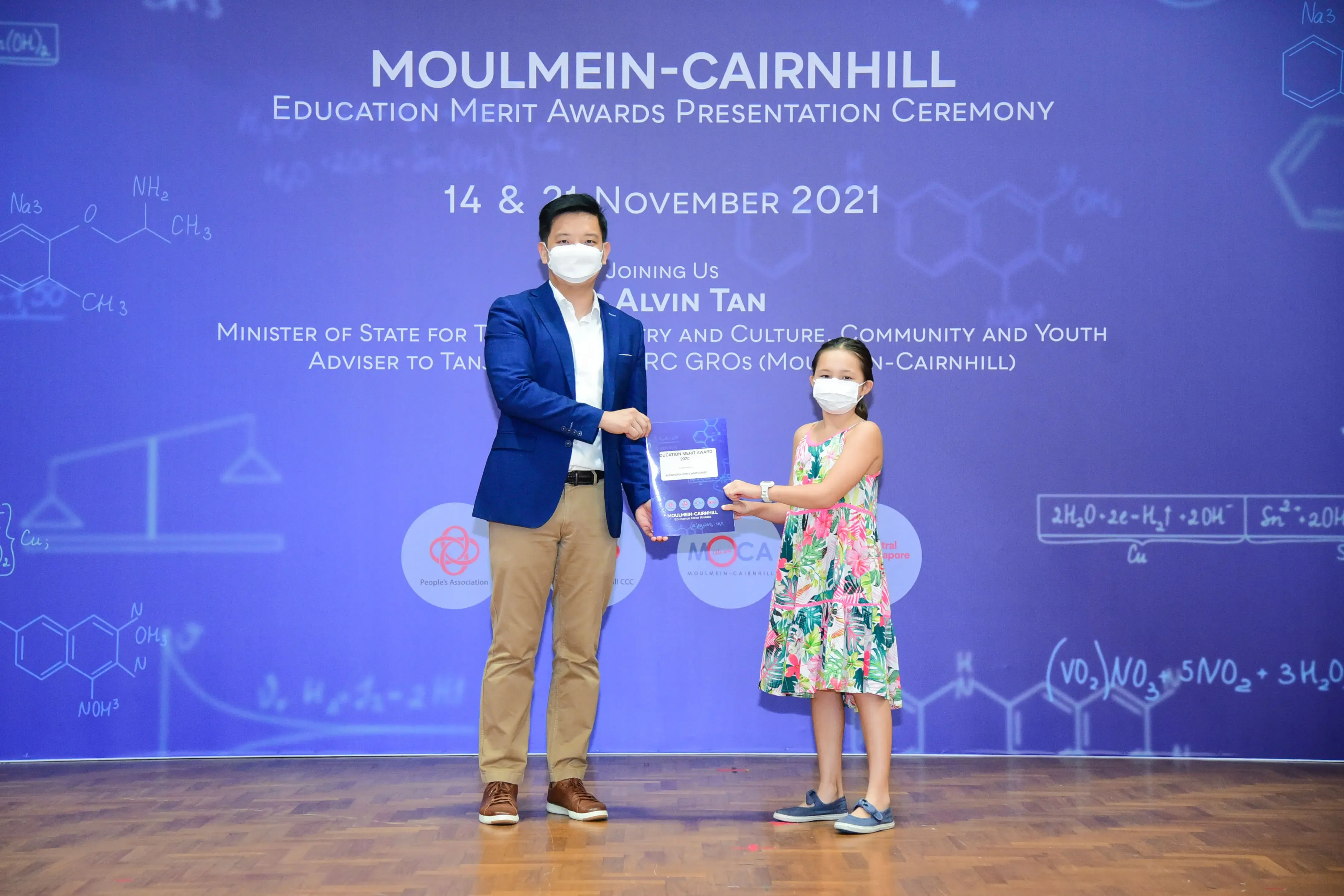 A man in a blue blazer presents an award to a young girl at the Moulmein-Cairnhill Education Merit Awards 2021.