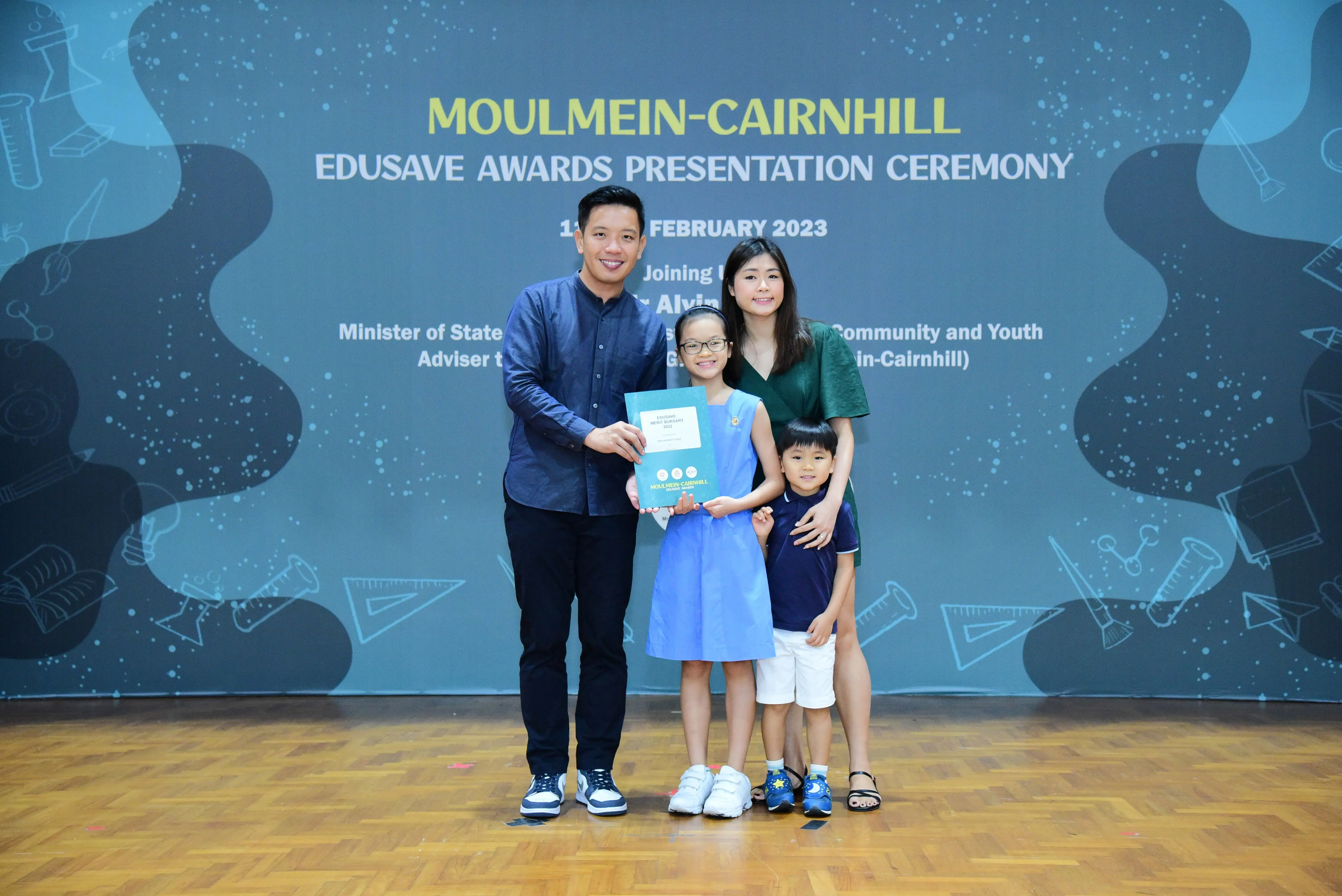 Family of four posing at the Moulmein-Cairnhill Edusave Awards Presentation Ceremony, girl holding a certificate.