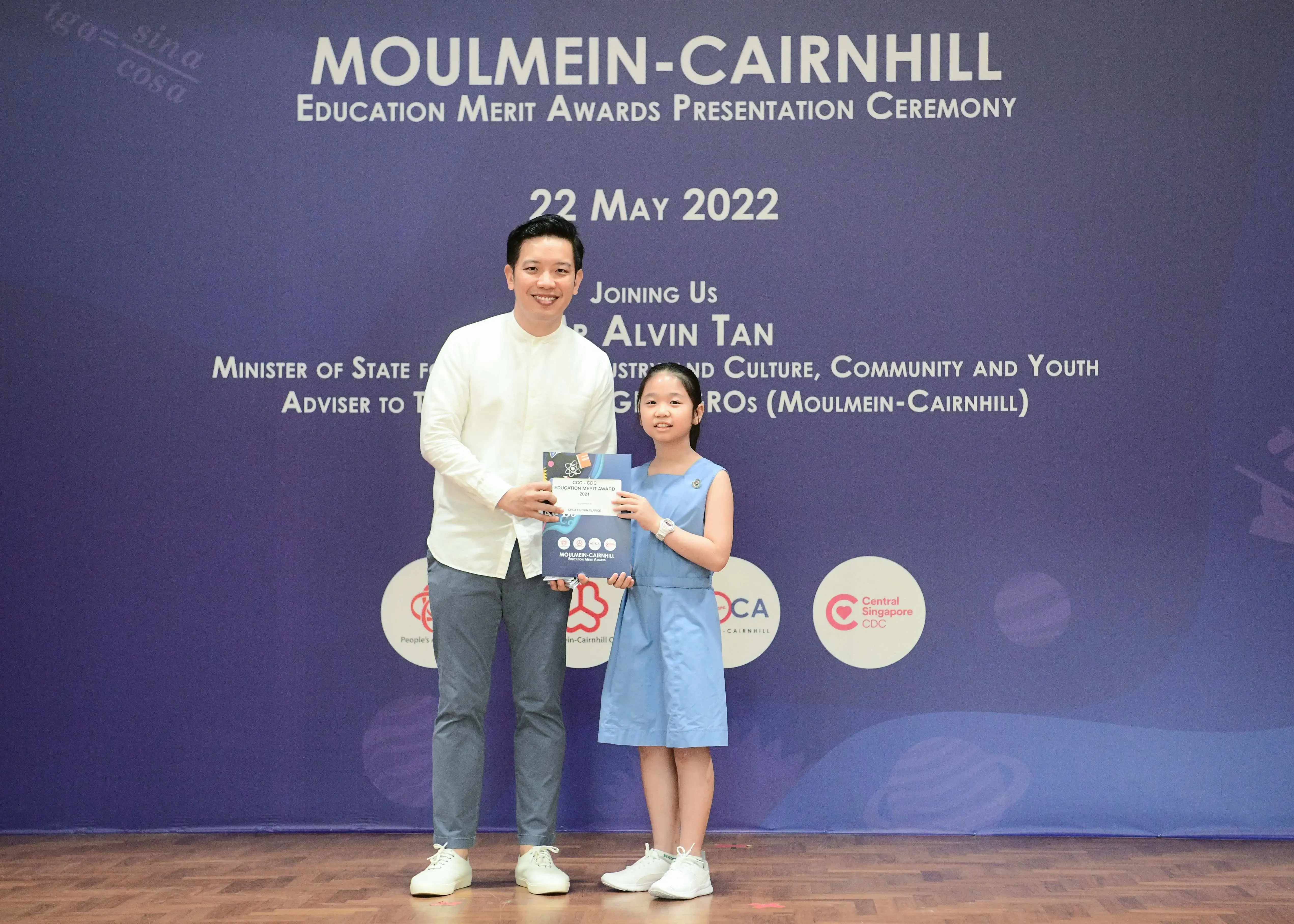 A man and a young girl hold award booklets at the Moulmein-Cairnhill Education Merit Awards Ceremony on 22 May 2022.