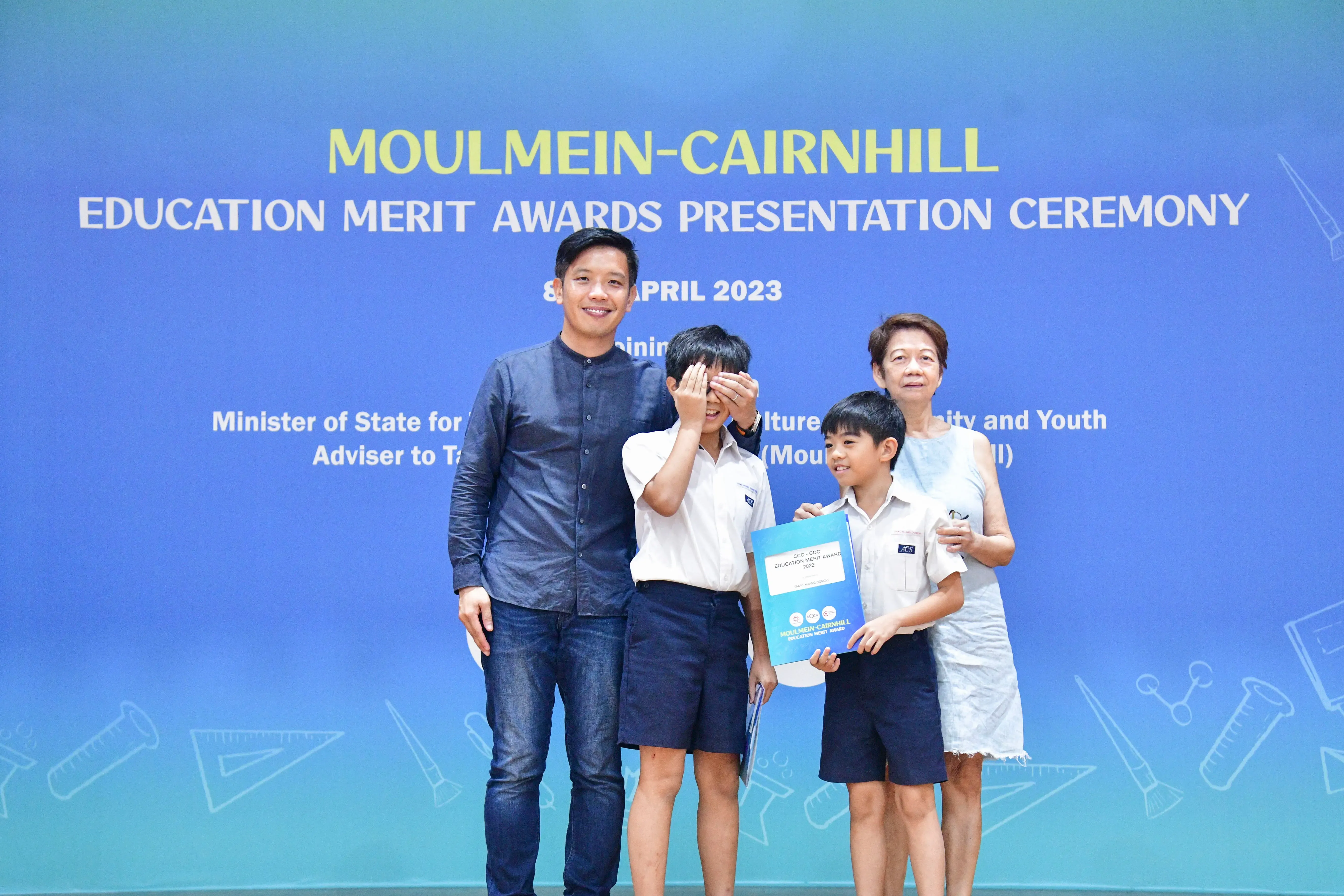 Two boys in school uniforms pose with a man and elderly woman at Moulmein-Cairnhill Education Merit Awards April 2023.