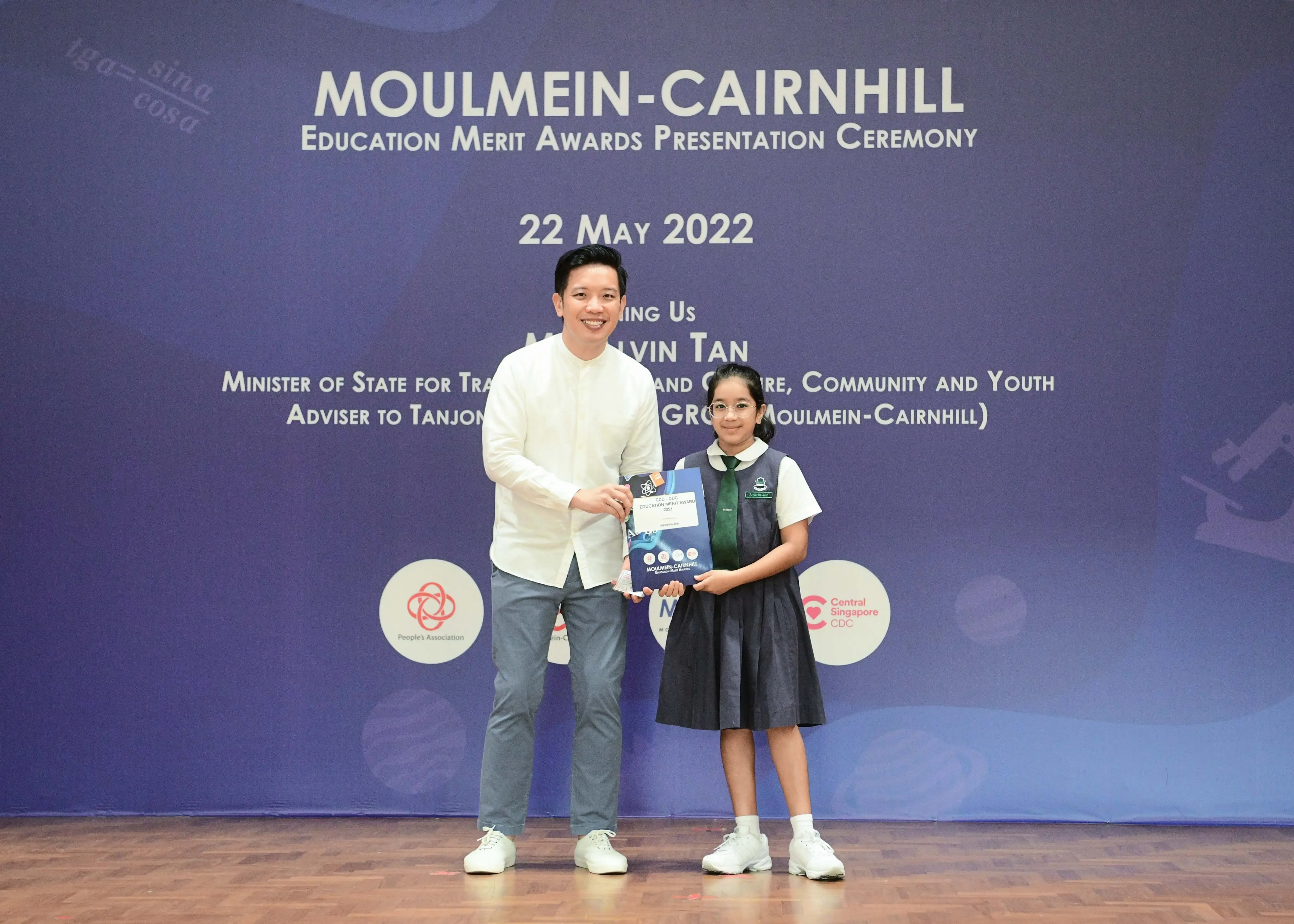 A man and a young girl in school uniform hold an award together at the Moulmein-Cairnhill Education Merit Awards 2022.