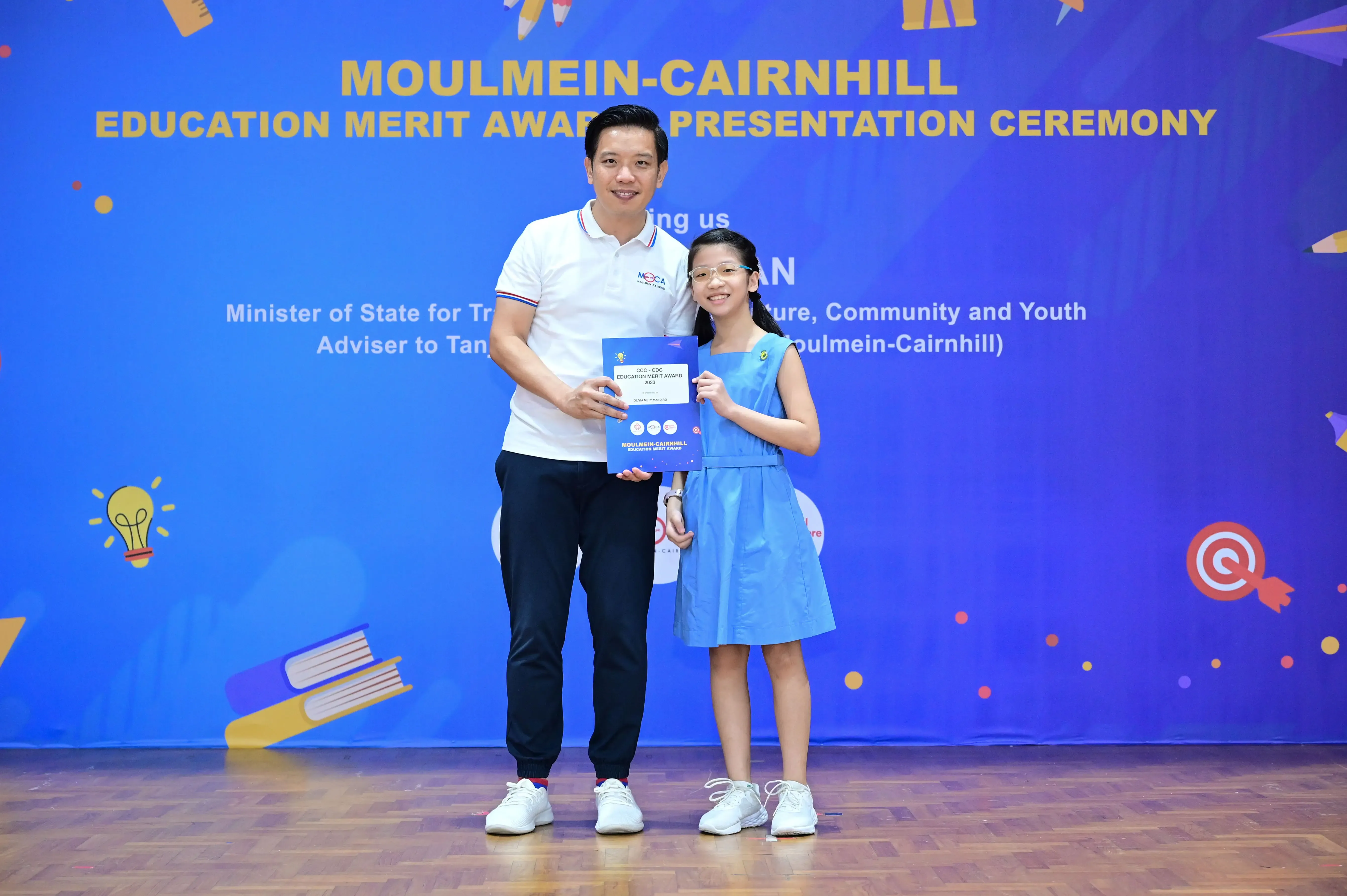 Man and young girl hold a blue certificate at the Moulmein-Cairnhill Education Merit Award Presentation Ceremony.