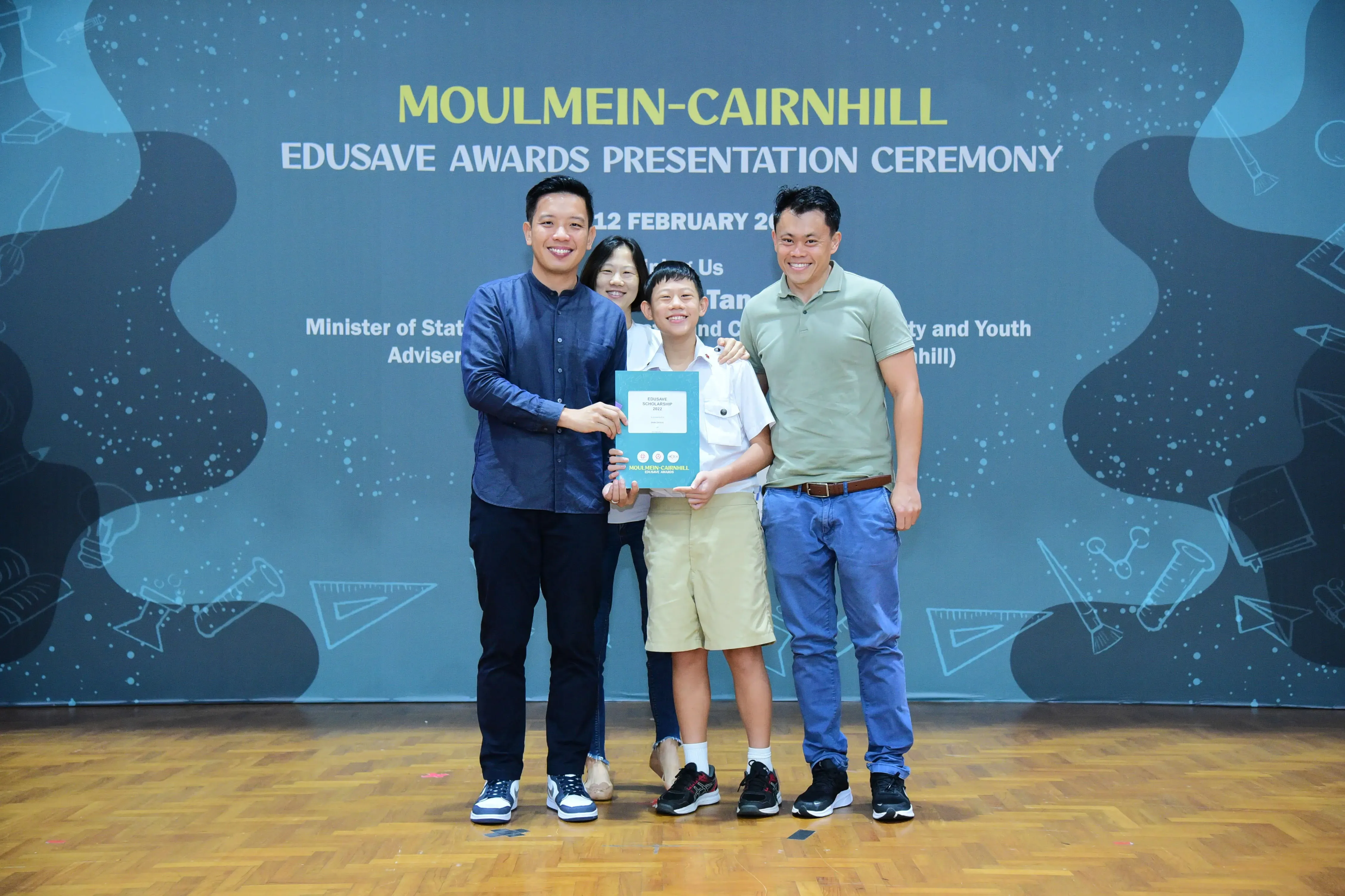 Four people smile while holding a certificate at the Moulmein-Cairnhill Edusave Awards Presentation Ceremony.