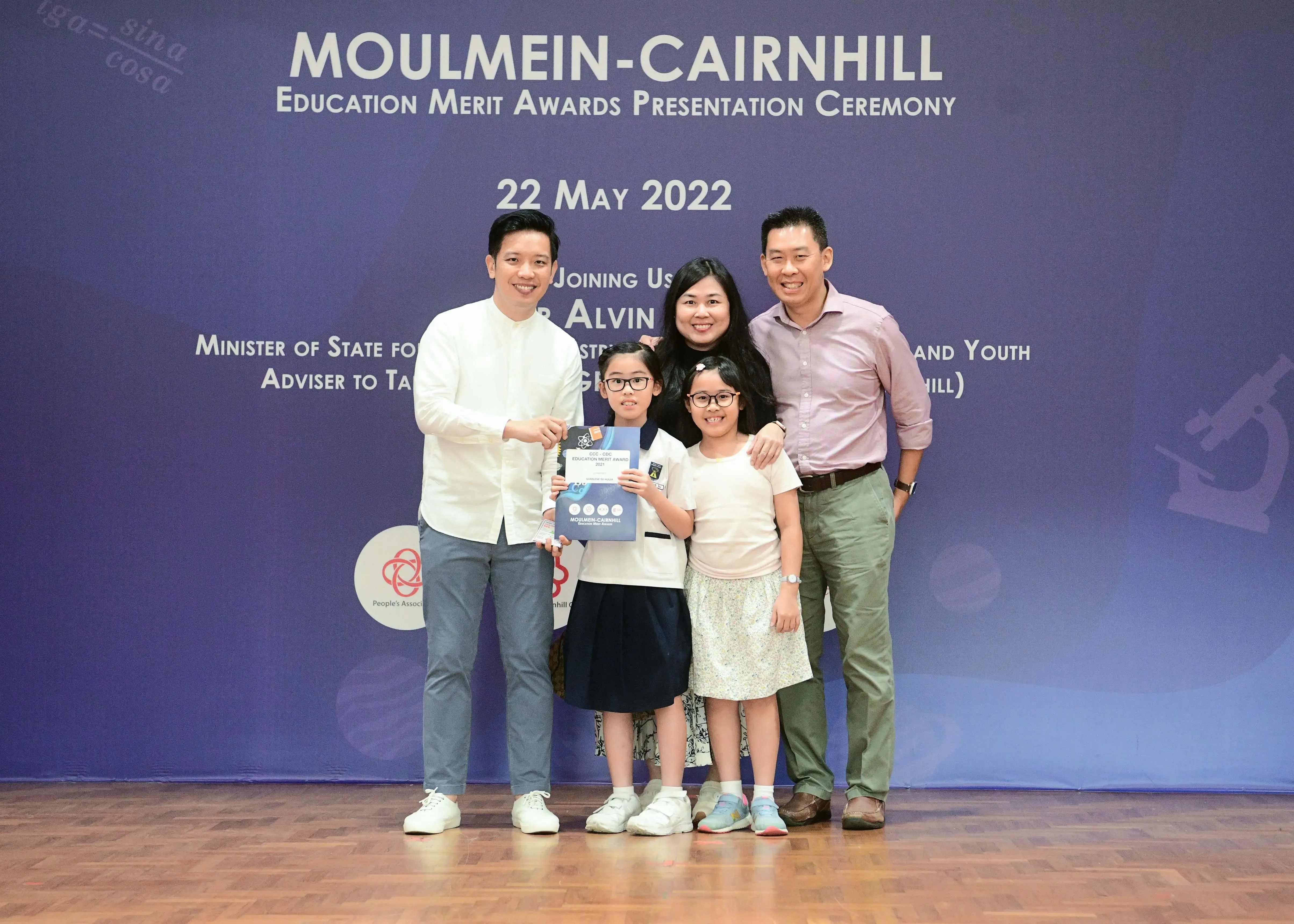Five people pose at the Moulmein-Cairnhill Education Merit Awards Ceremony on 22 May 2022, two girls holding an award.