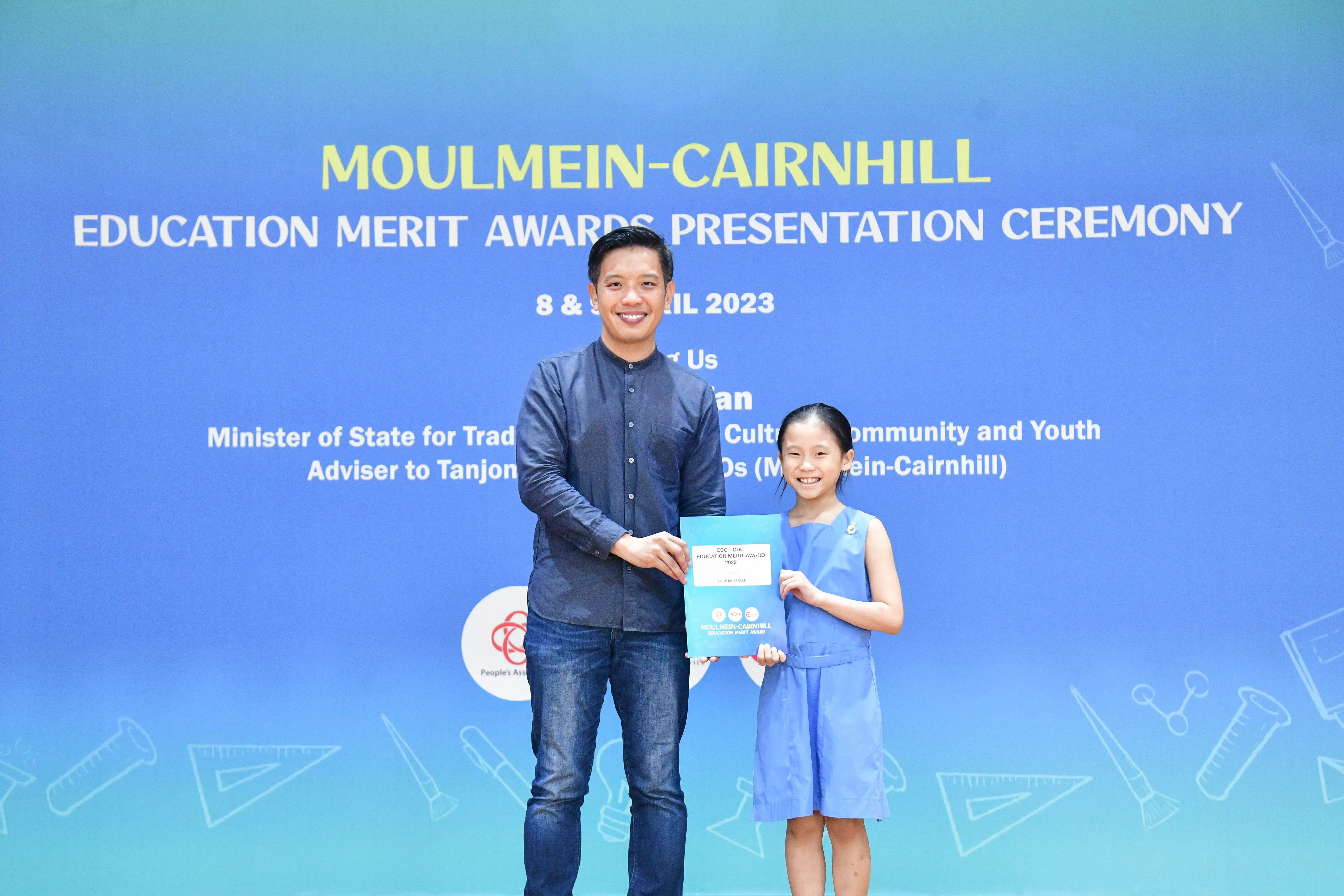 A man and a young girl hold an award certificate at the Moulmein-Cairnhill Education Merit Awards Ceremony 2023.