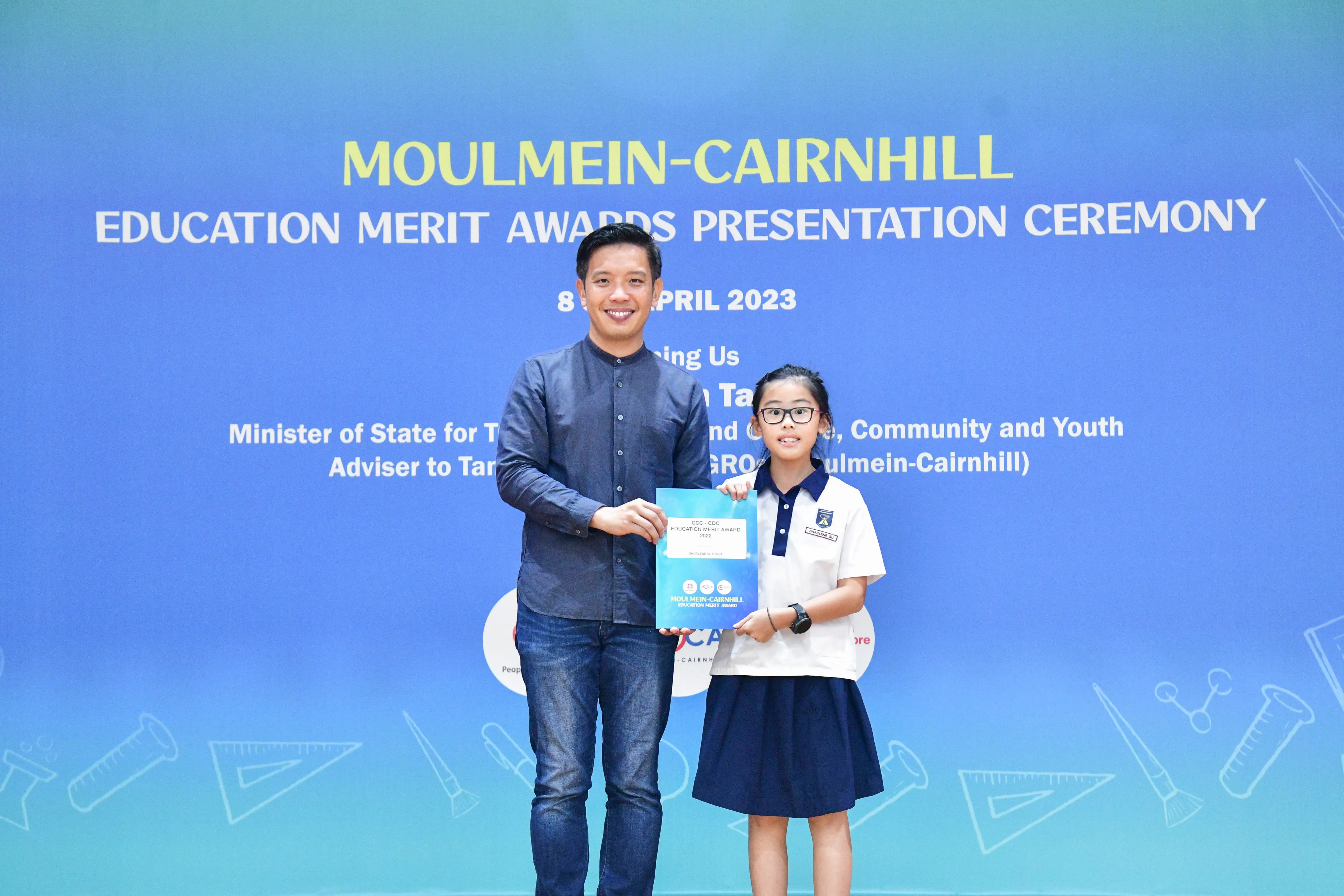 A man and a young girl in school uniform hold an award certificate at the Moulmein-Cairnhill Education Merit Awards 2023.