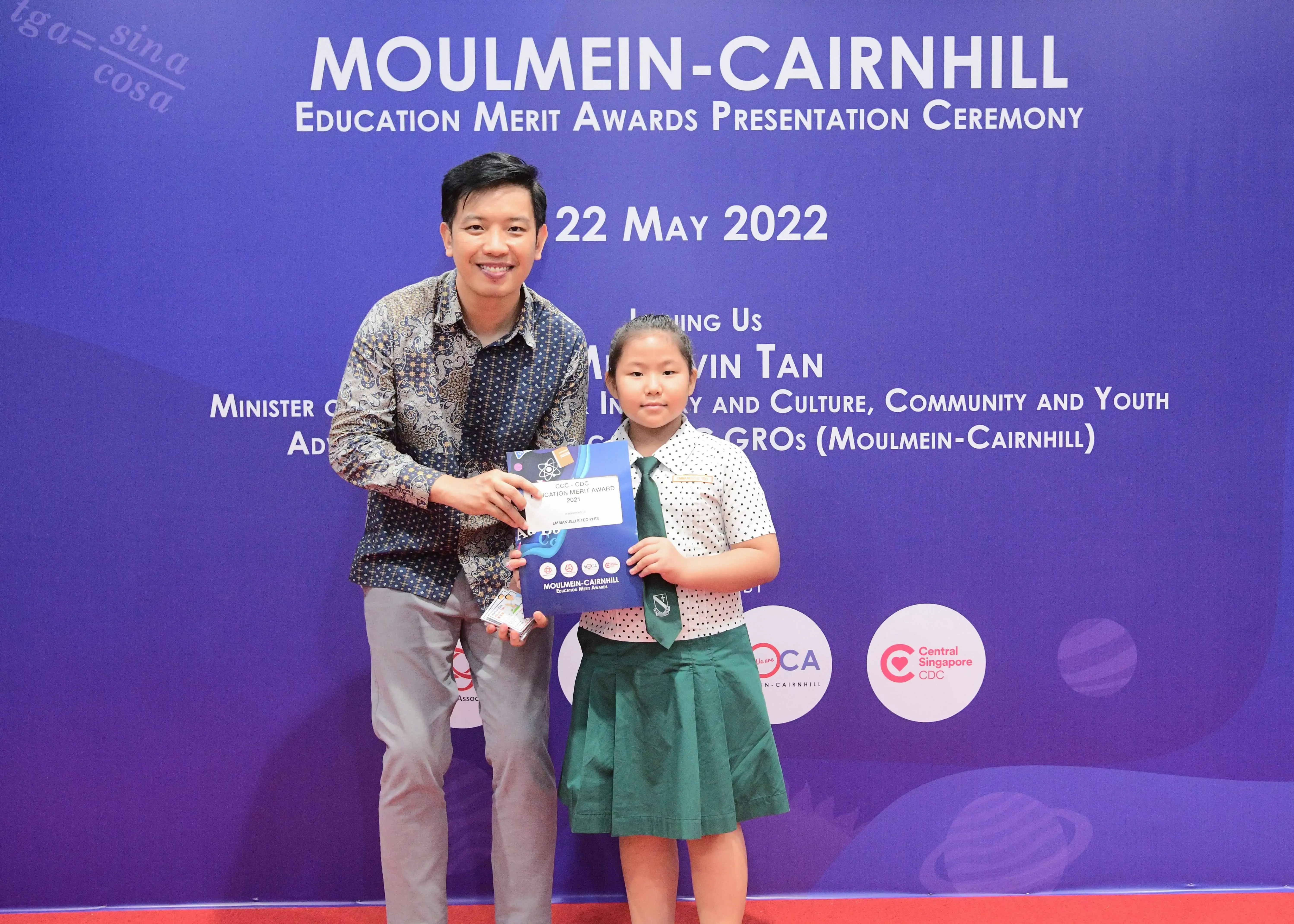 A man and a young girl in school uniform hold an award certificate at the Moulmein-Cairnhill Education Merit Awards 2022.