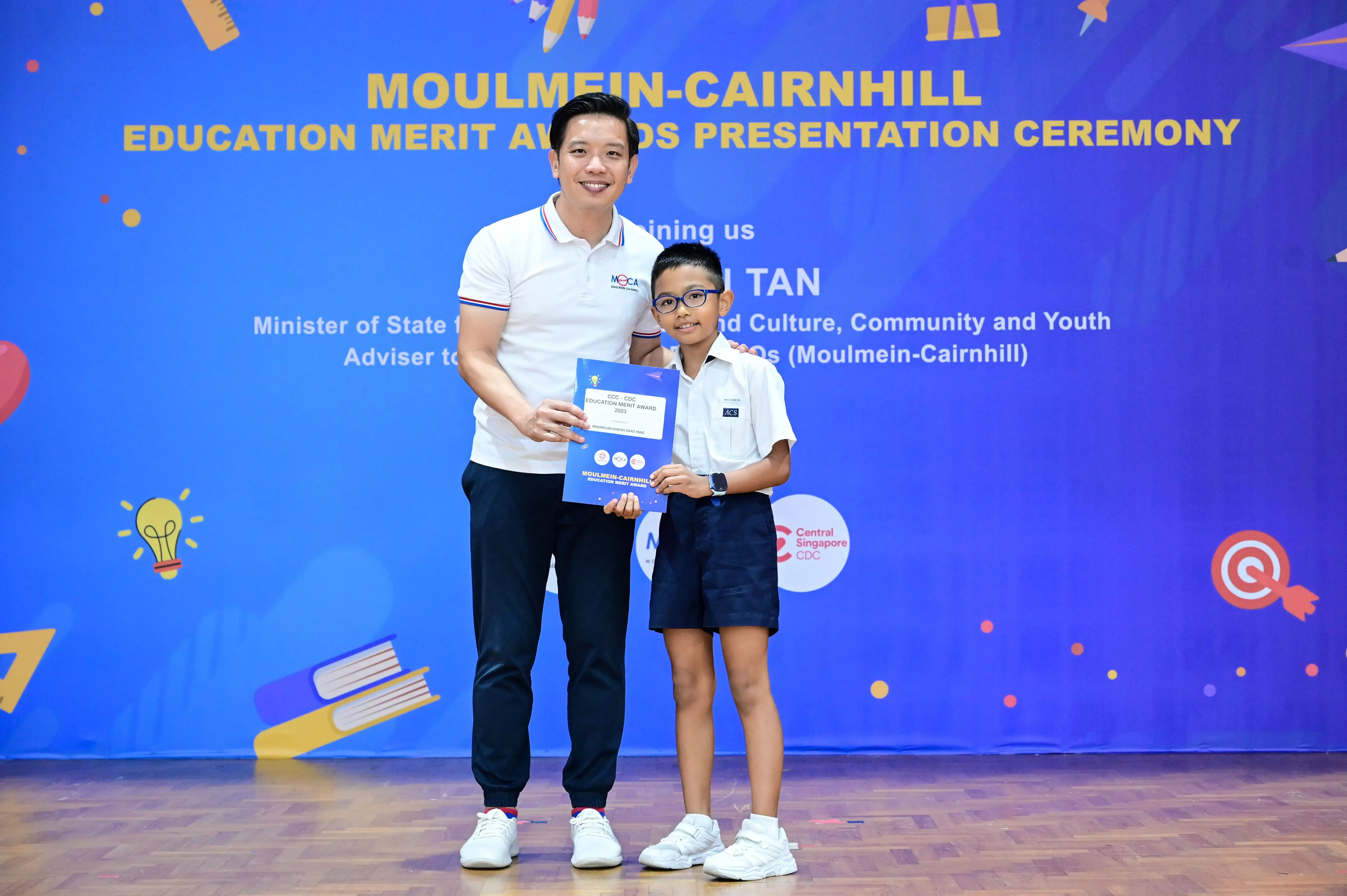 A man and a young boy hold a certificate at the Moulmein-Cairnhill Education Merit Awards Presentation Ceremony.