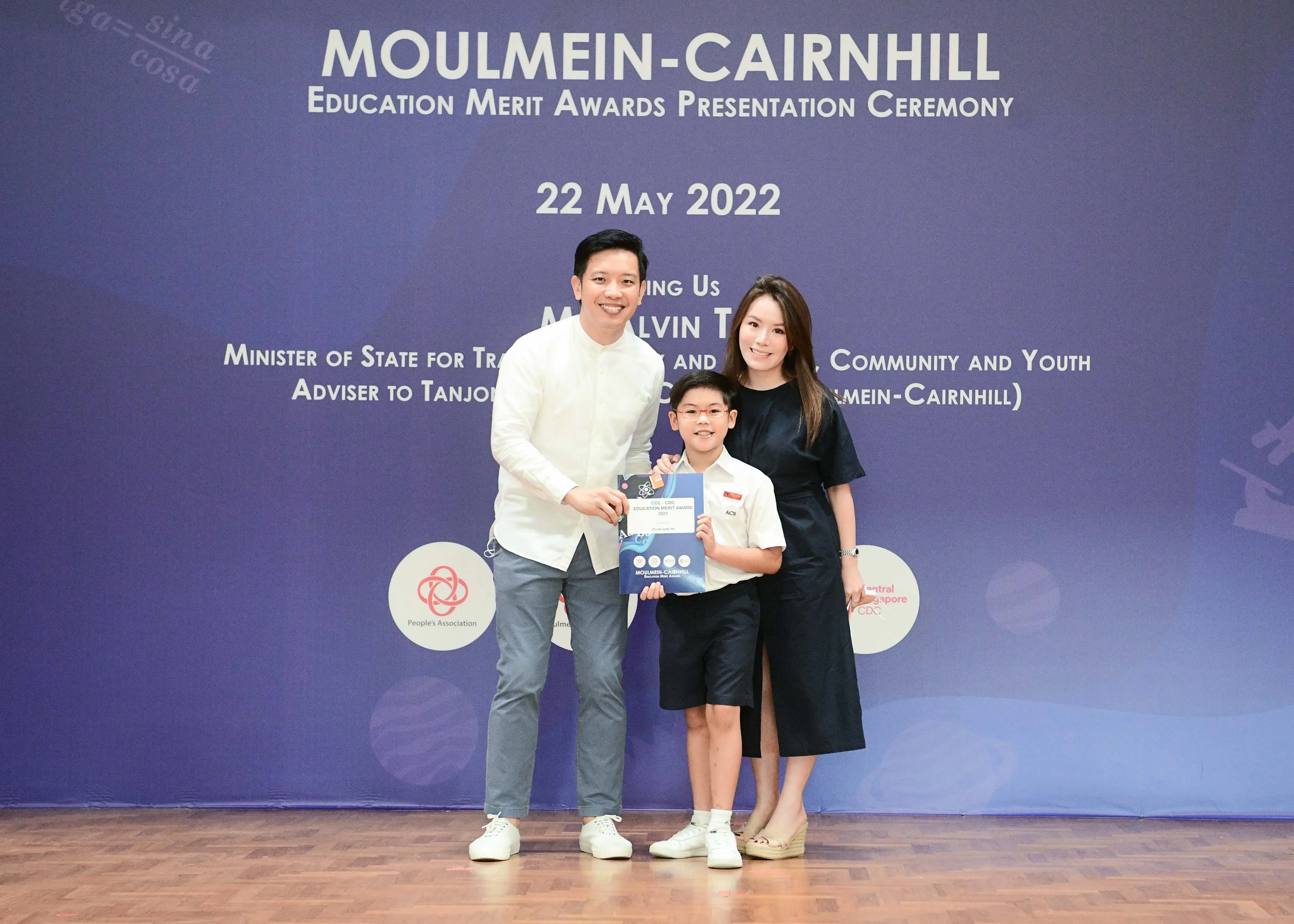 Two adults and a child pose with an award booklet at the Moulmein-Cairnhill Education Merit Awards, 22 May 2022.