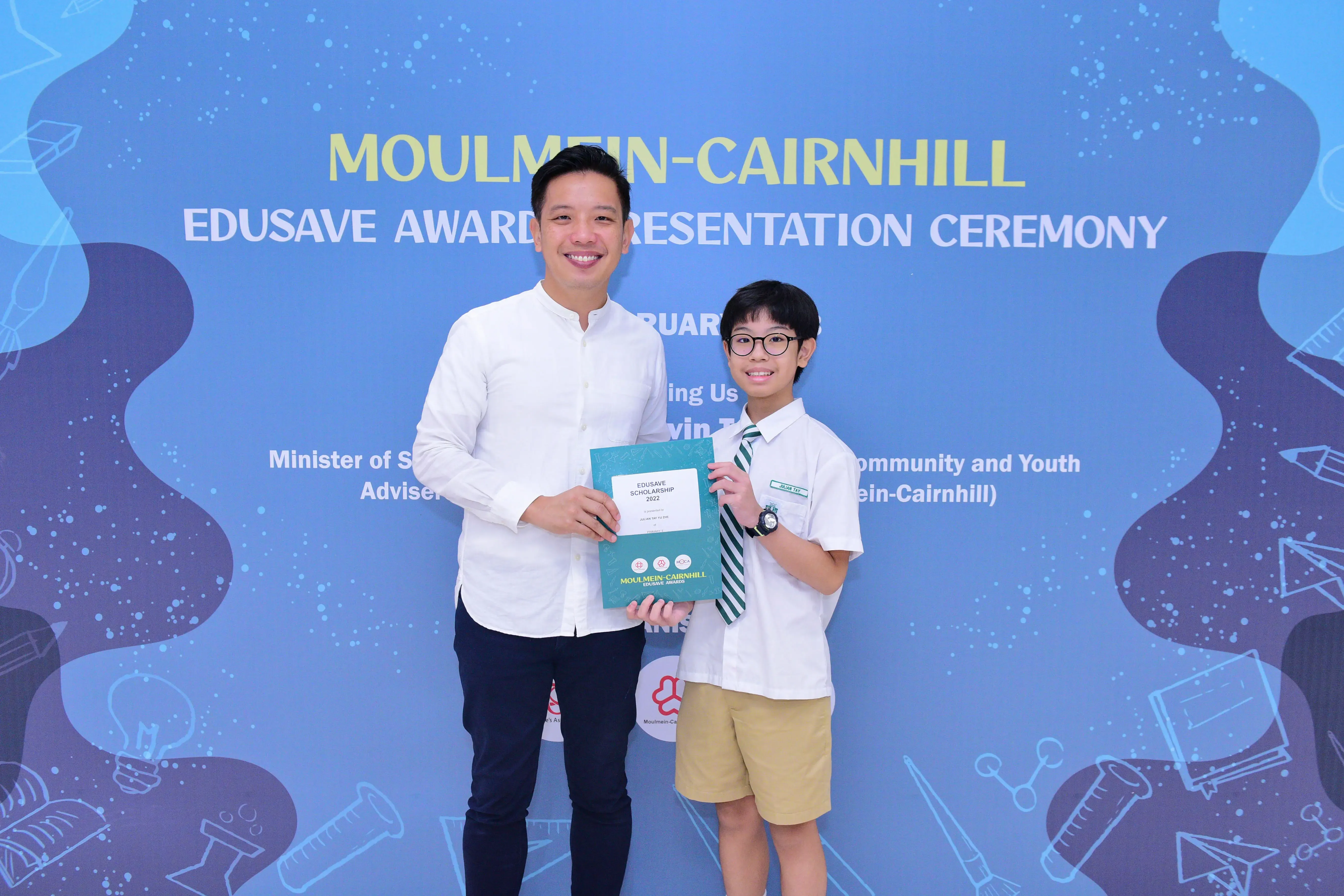 An adult and a young student in uniform hold an Edusave Scholarship certificate at the Moulmein-Cairnhill Awards Ceremony.