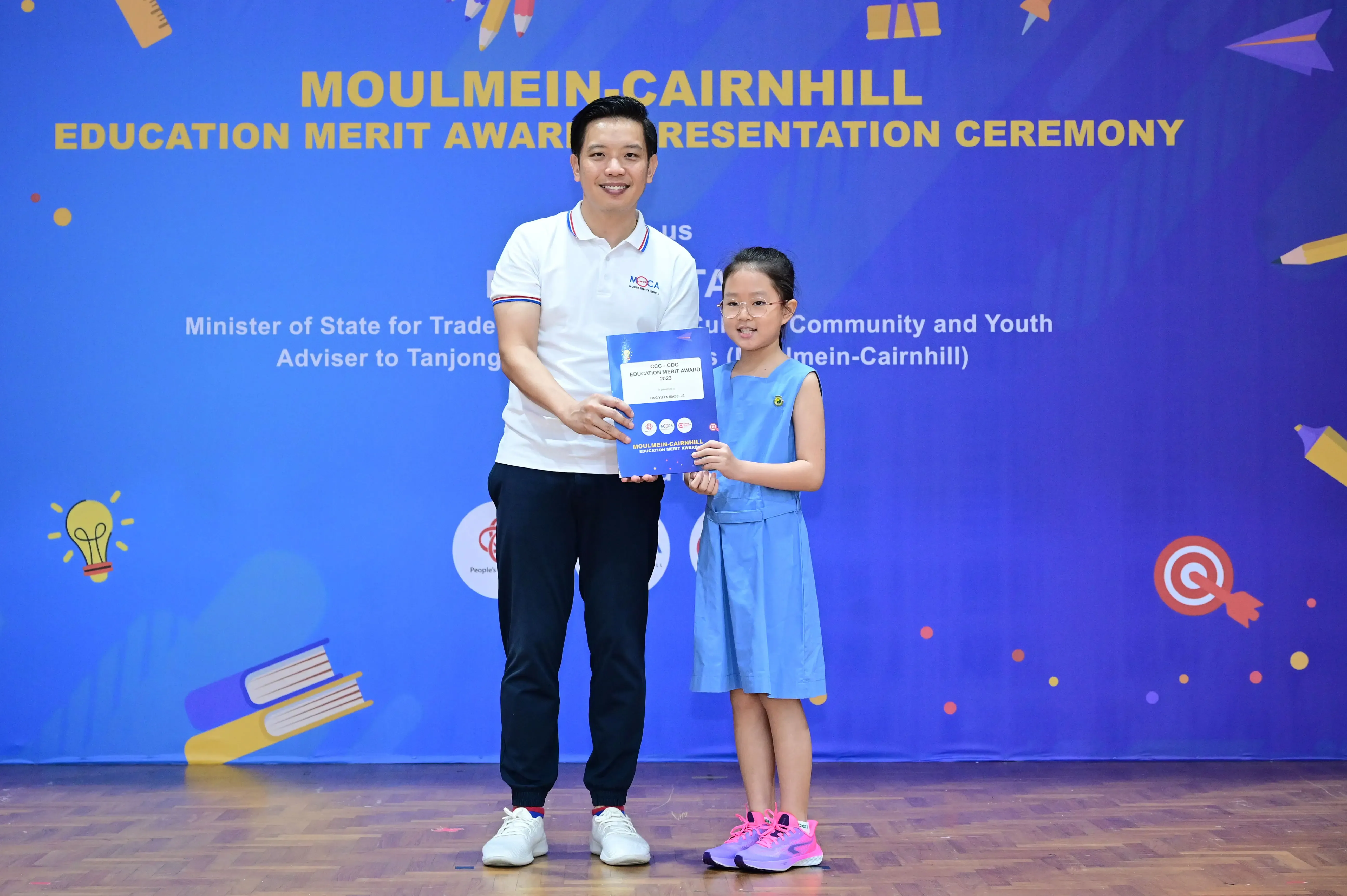A man and a young girl hold a certificate together at the Moulmein-Cairnhill Education Merit Award Presentation Ceremony.