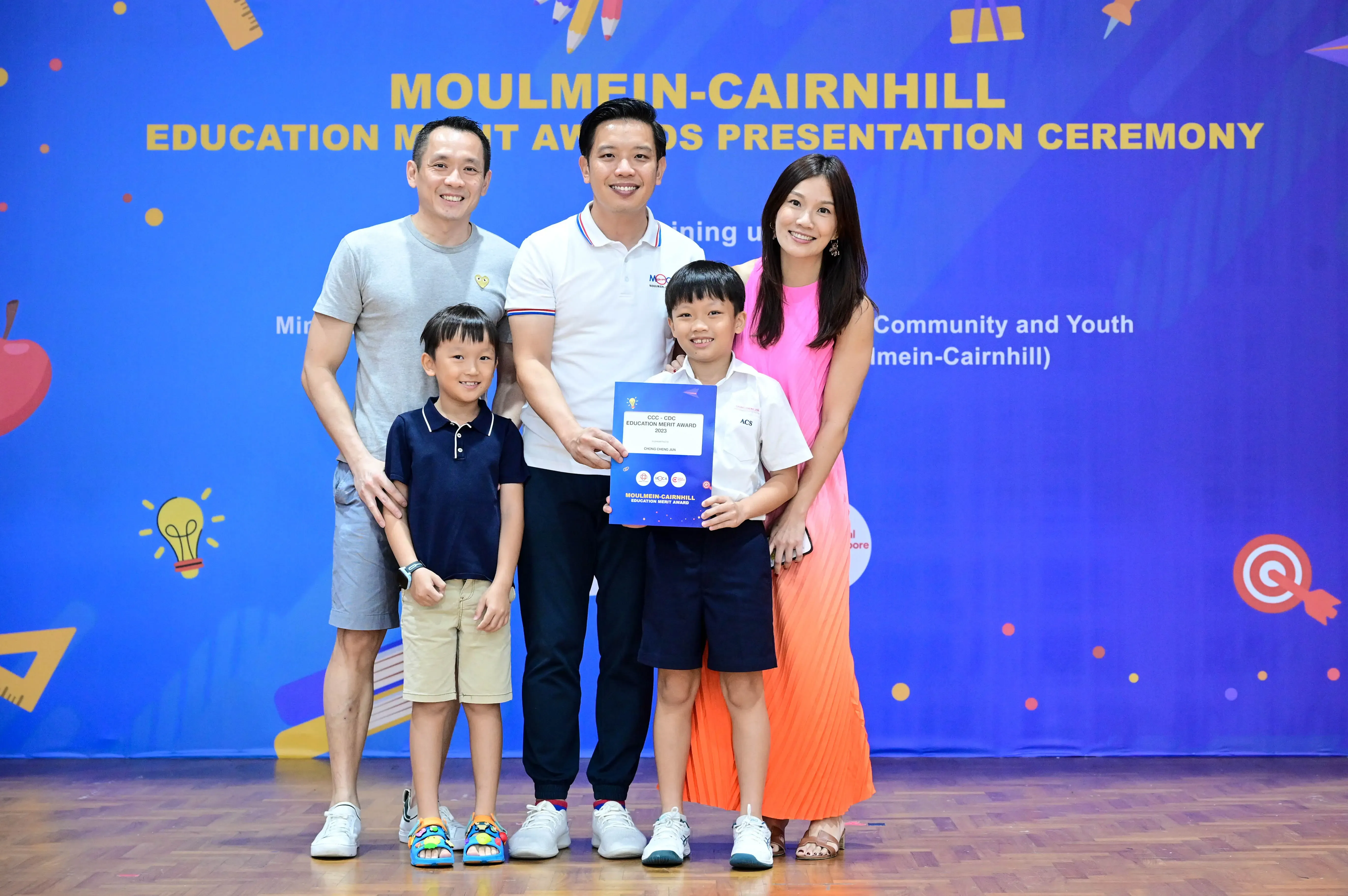 Two adults and two children pose with a certificate at the Moulmein-Cairnhill Education Merit Awards Presentation Ceremony.
