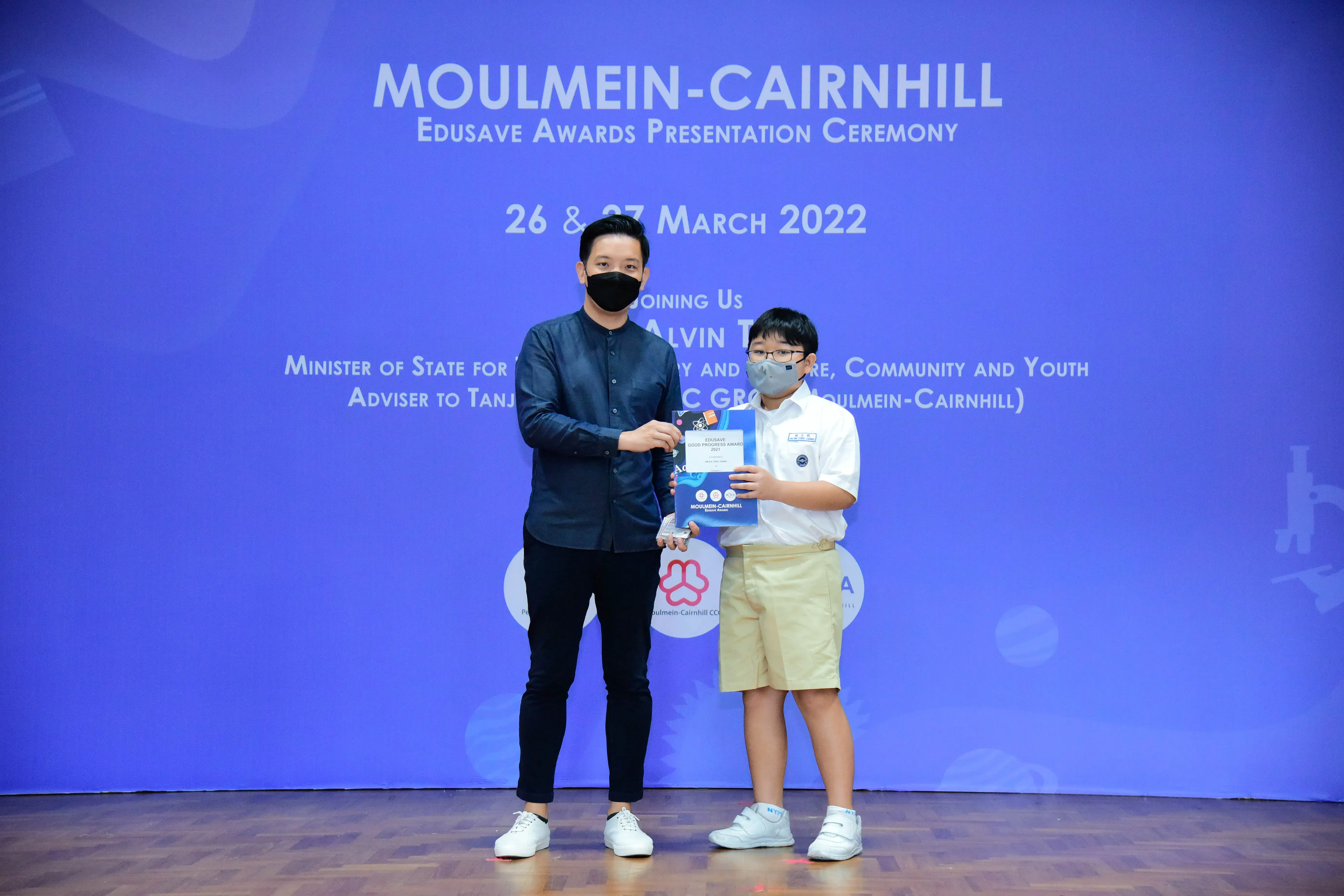 An adult and a young boy in masks hold an award at the Moulmein-Cairnhill Edusave Awards Ceremony 2022.