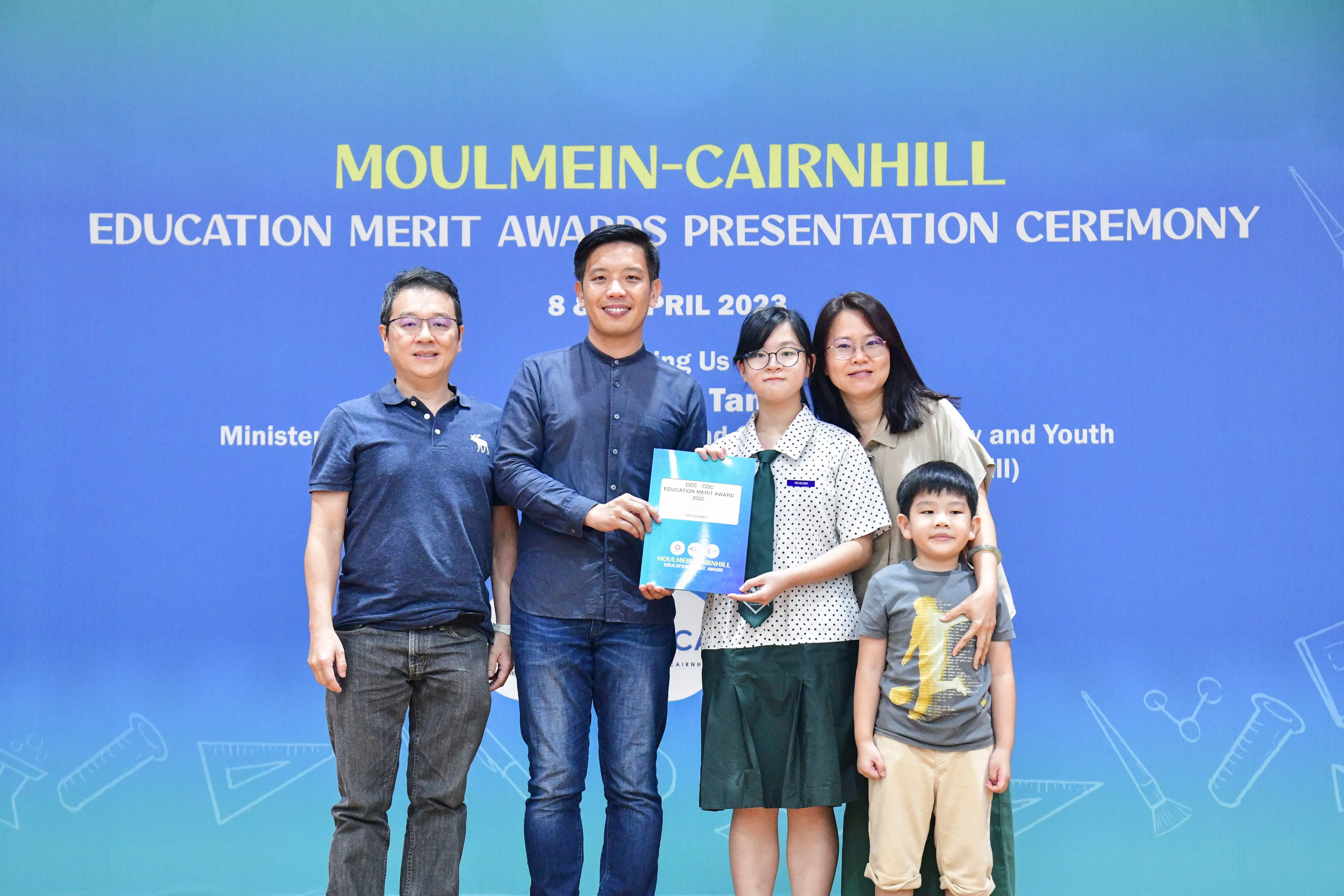 Five people pose at the Moulmein-Cairnhill Education Merit Awards Ceremony, with a student holding a certificate.