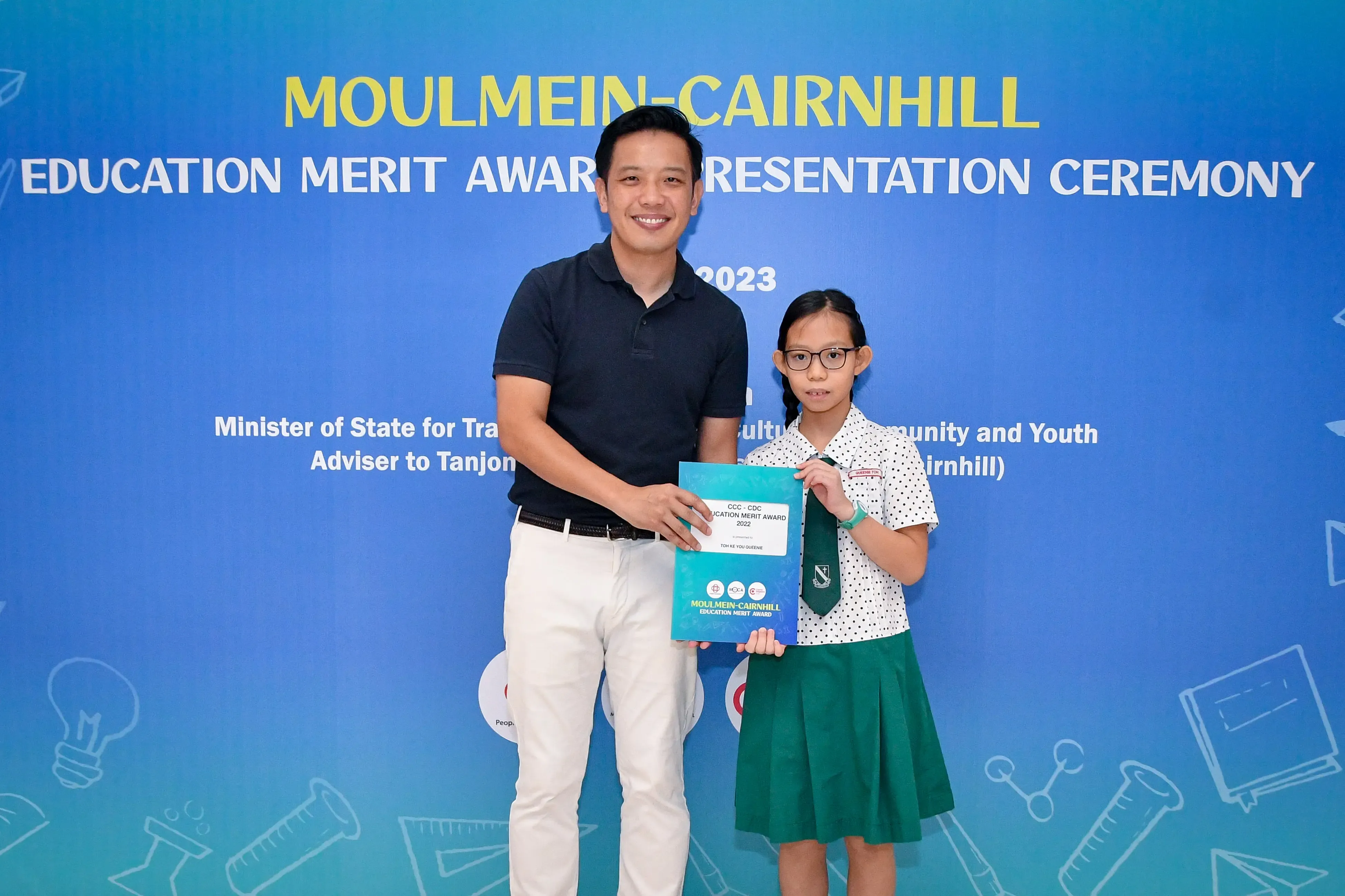 Man and young girl hold a certificate at the Moulmein-Cairnhill Education Merit Award Presentation Ceremony 2023.