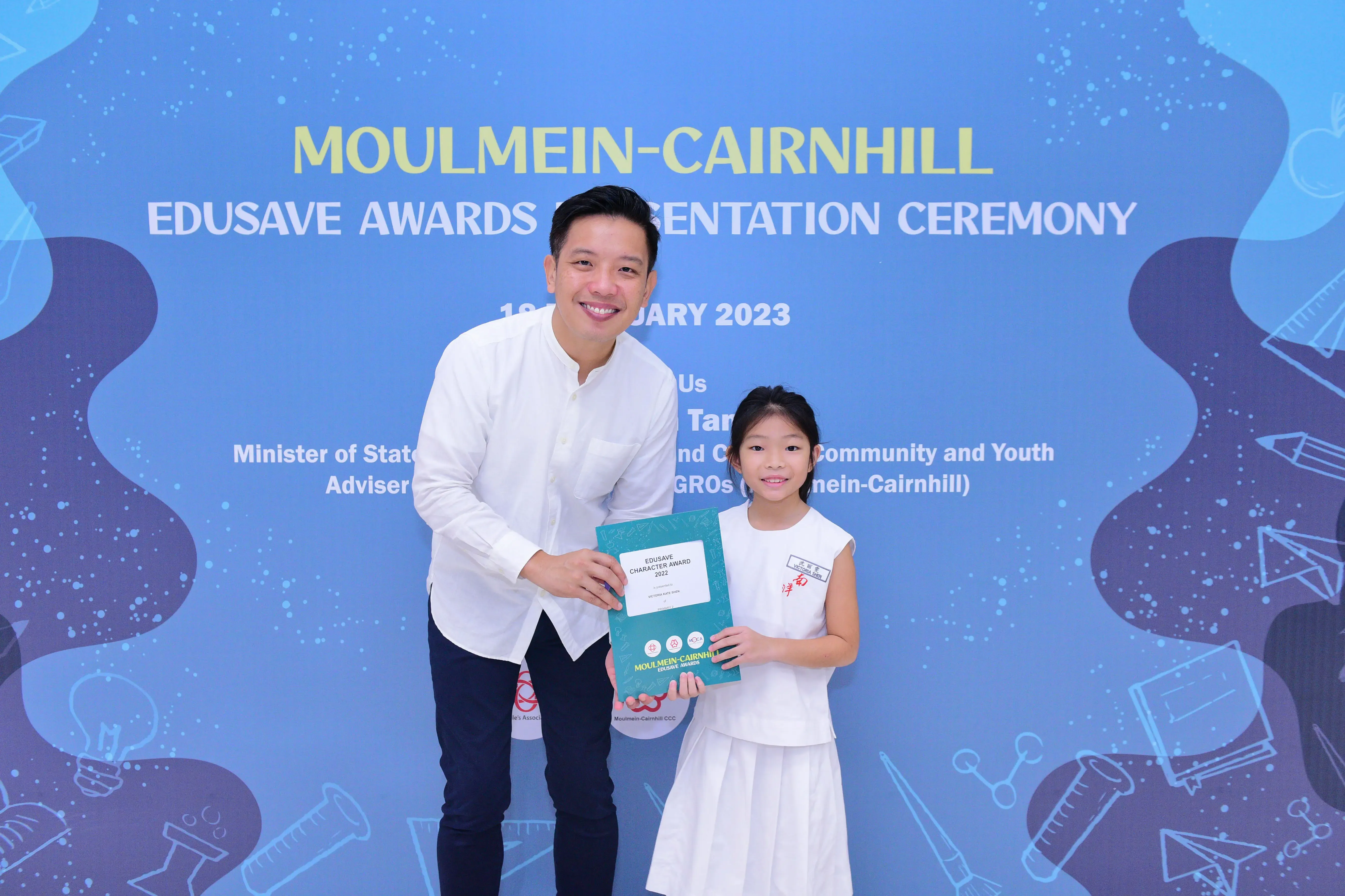 A man and a young girl hold a teal award folder at the Moulmein-Cairnhill Edusave Awards Ceremony 2023.