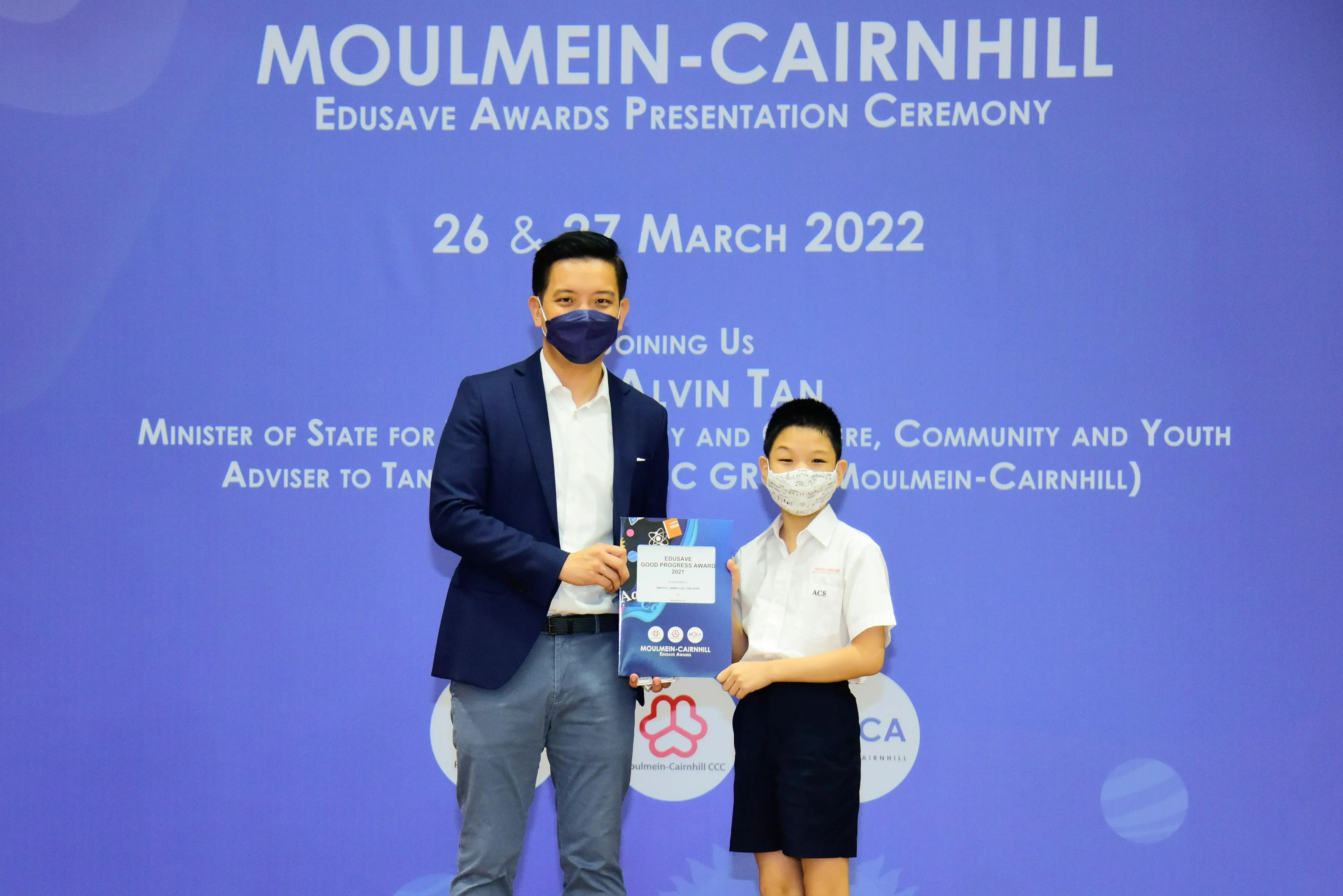 An adult and a young student in masks hold an award at the Moulmein-Cairnhill Edusave Awards Ceremony, March 2022.