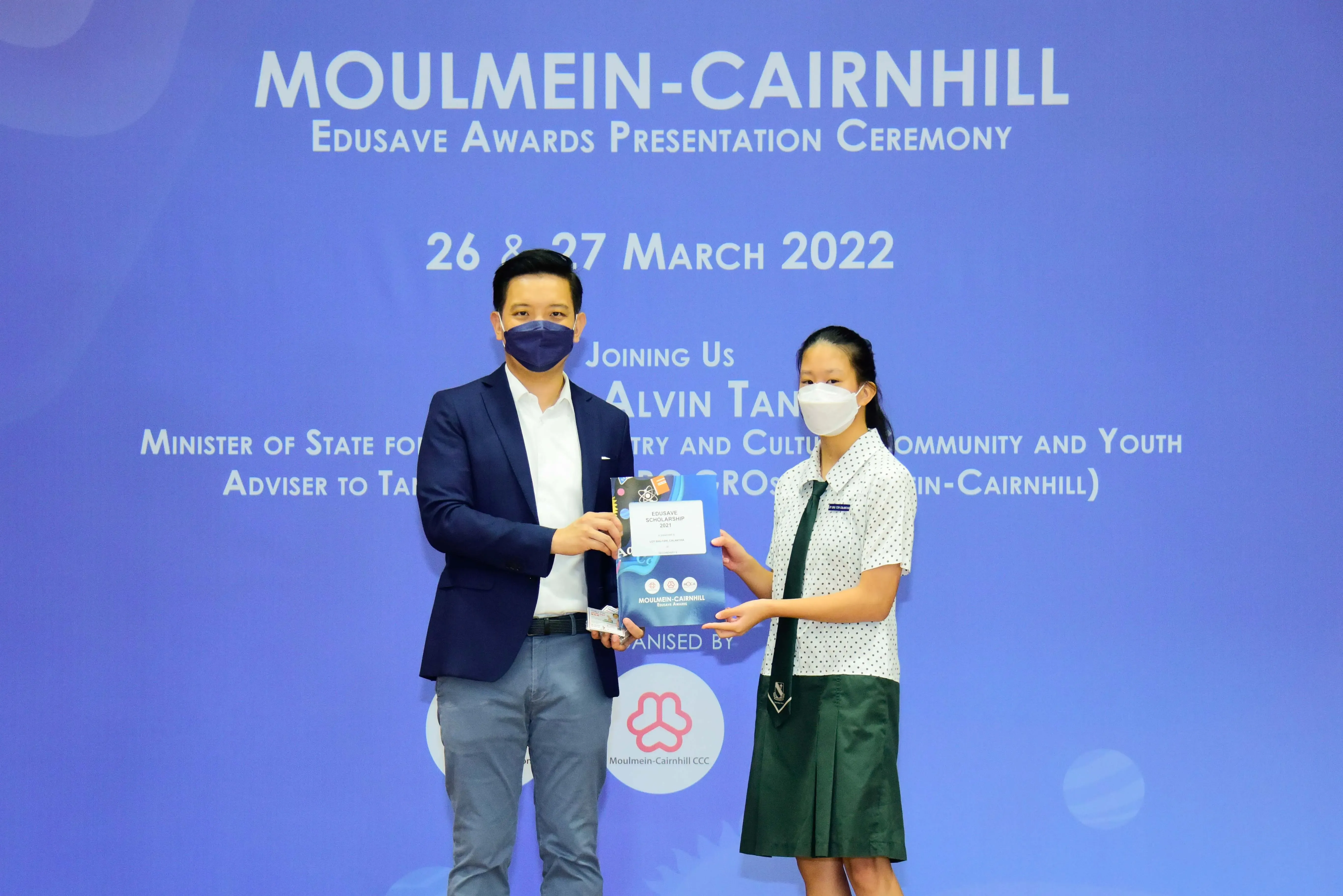 A man and a student in uniform, both masked, hold a certificate at the Moulmein-Cairnhill Edusave Awards Ceremony 2022.