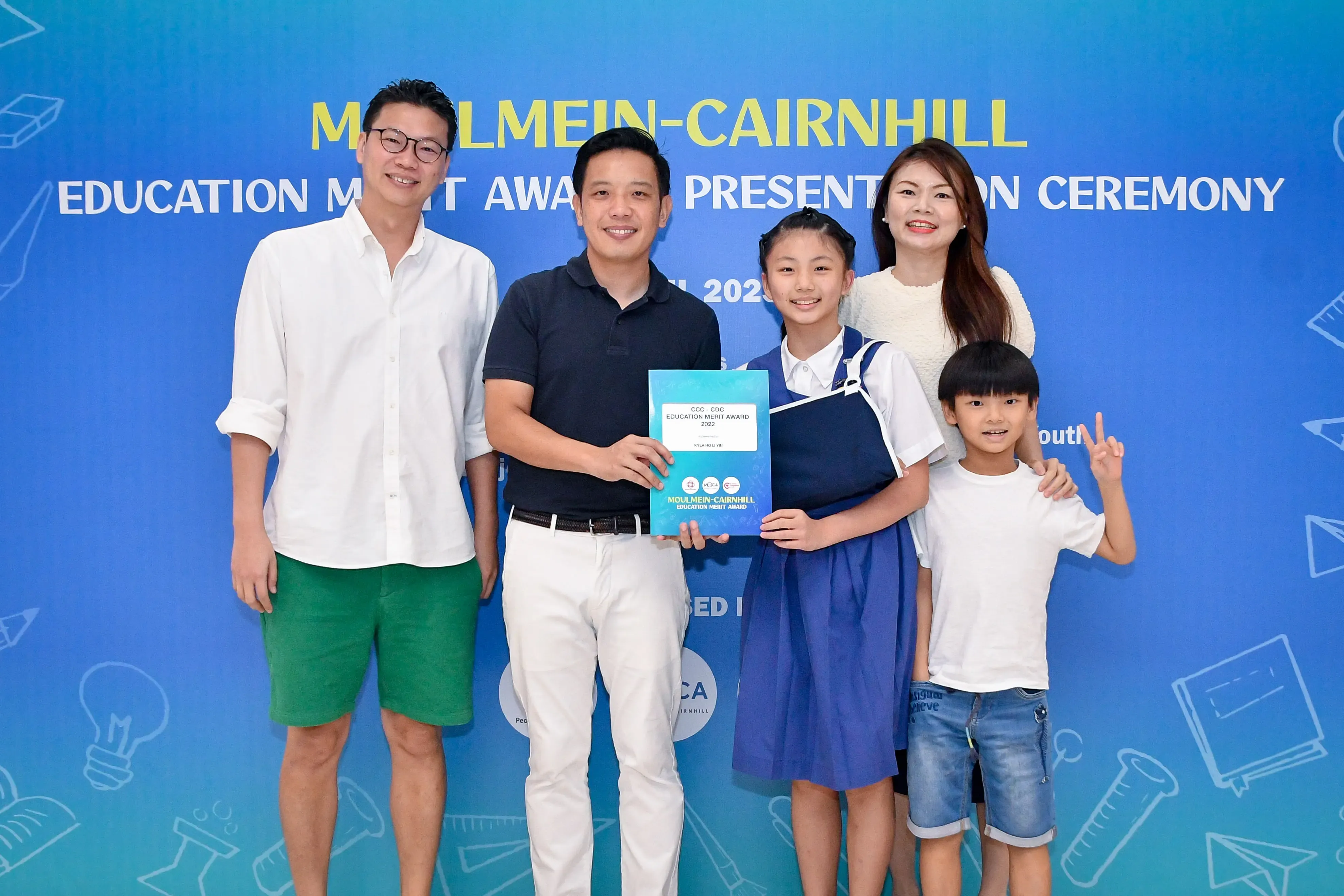 Five people pose at the Moulmein-Cairnhill Education Merit Award Presentation Ceremony, holding a certificate.