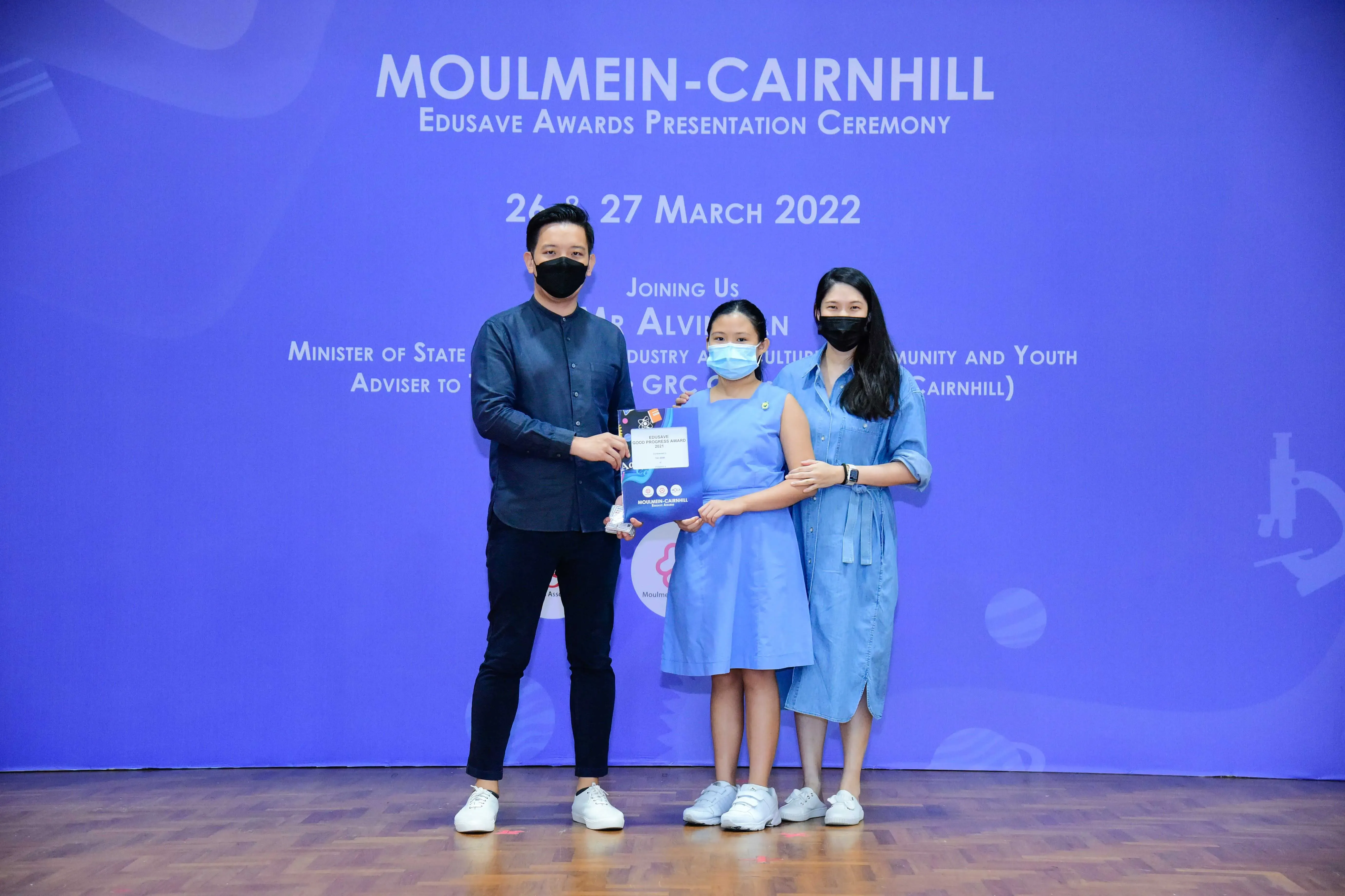 Three masked people pose with an award at the Moulmein-Cairnhill Edusave Awards Ceremony, March 2022.