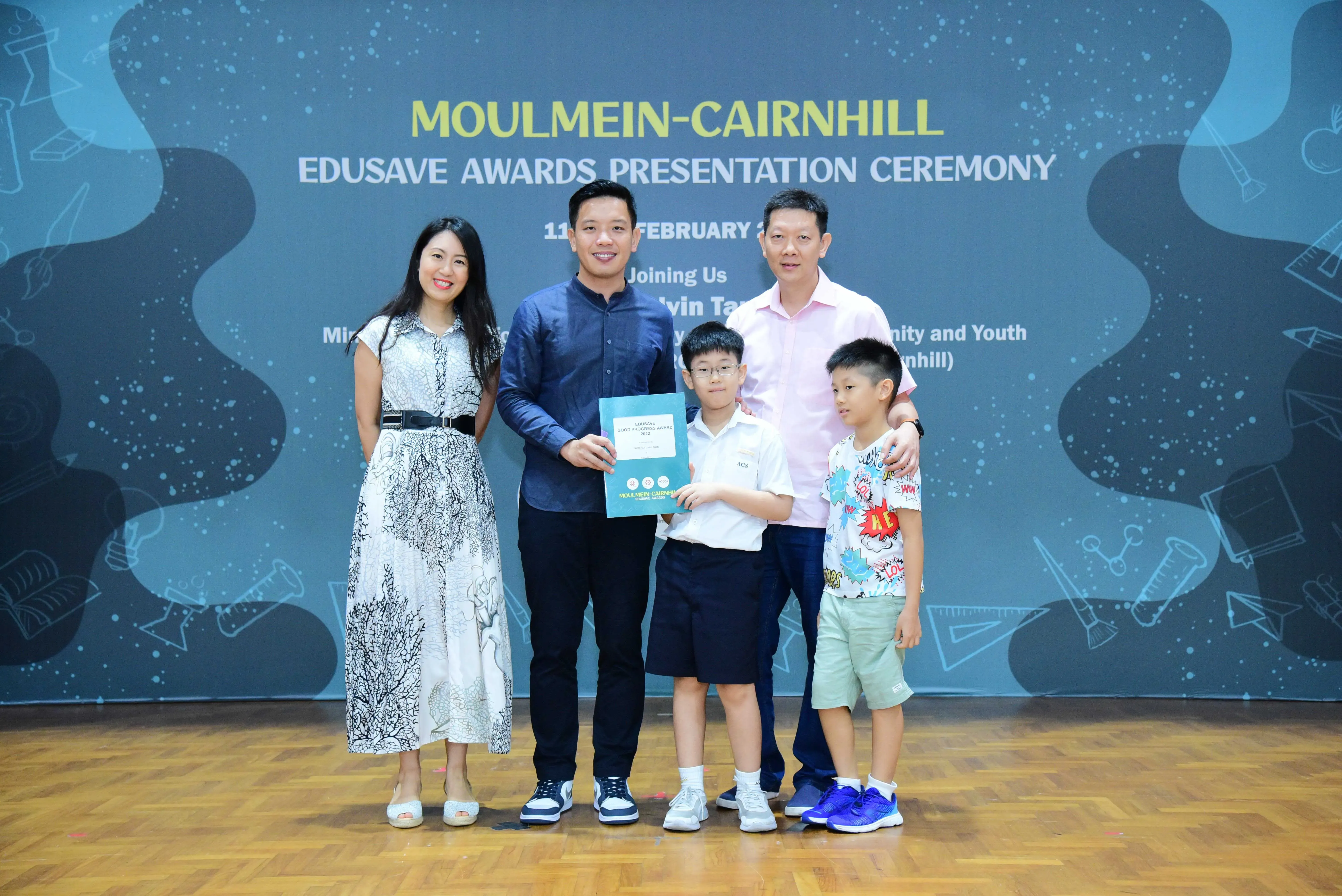 Five people pose with an award certificate at the Moulmein-Cairnhill Edusave Awards Presentation Ceremony backdrop.